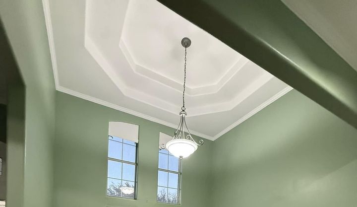 Green room with a high coffered ceiling, hanging light, and two tall windows