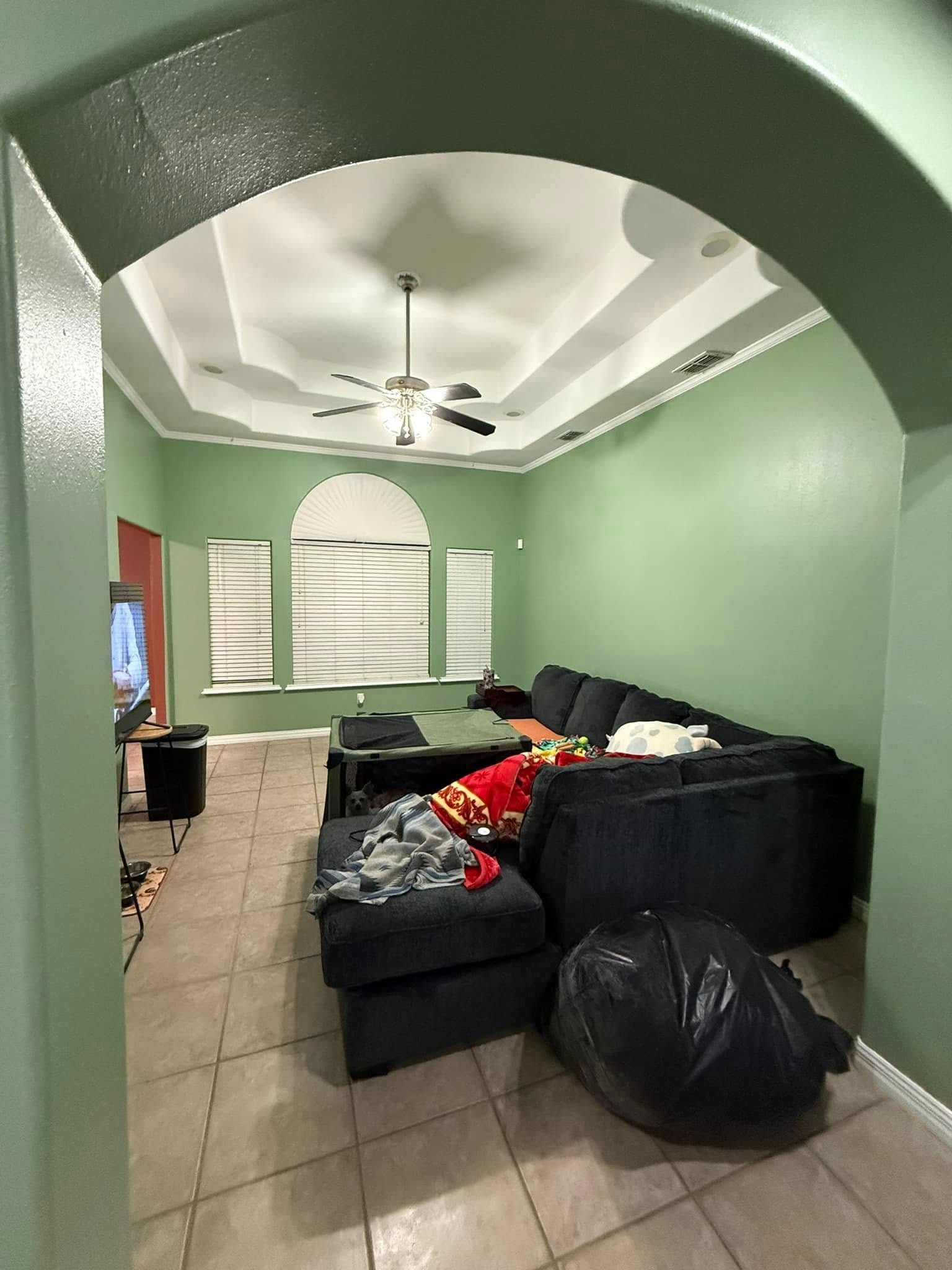 Green living room with black sectional sofa, tiled floor, ceiling fan, and arched doorway.