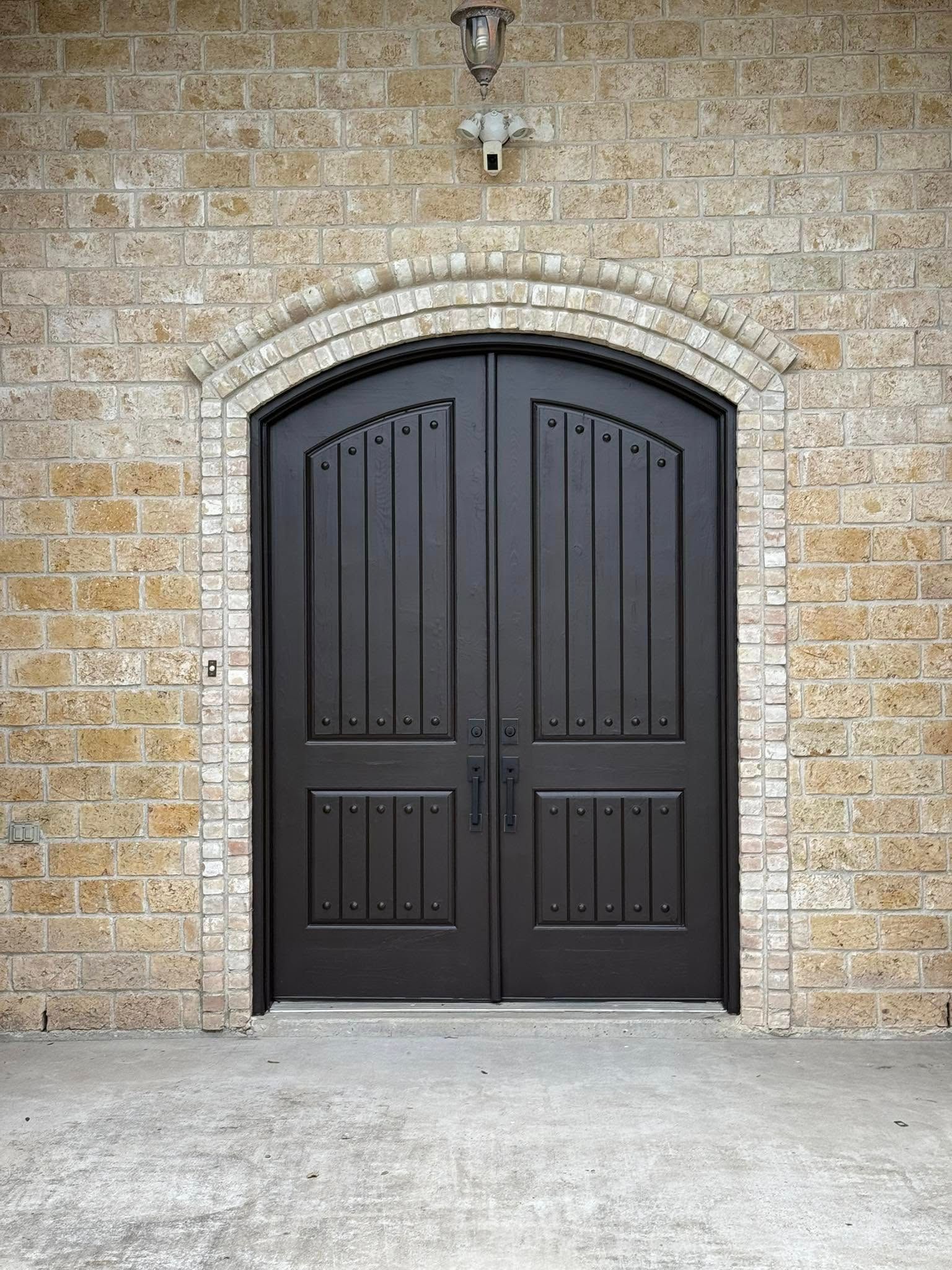 Dark wooden double door set in a beige brick wall with an arched frame.