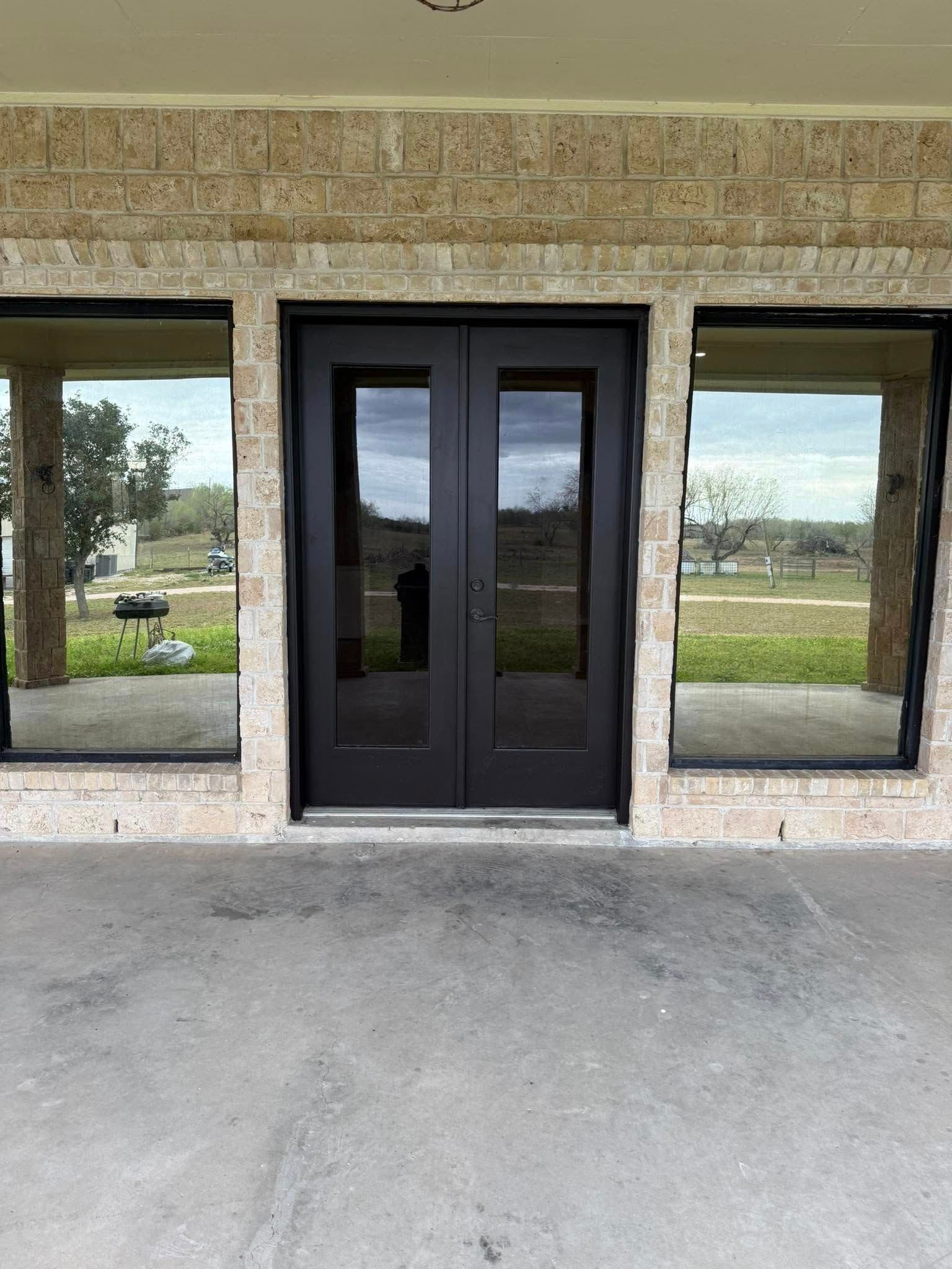 Black double glass doors centered between two large windows on a stone building facade.