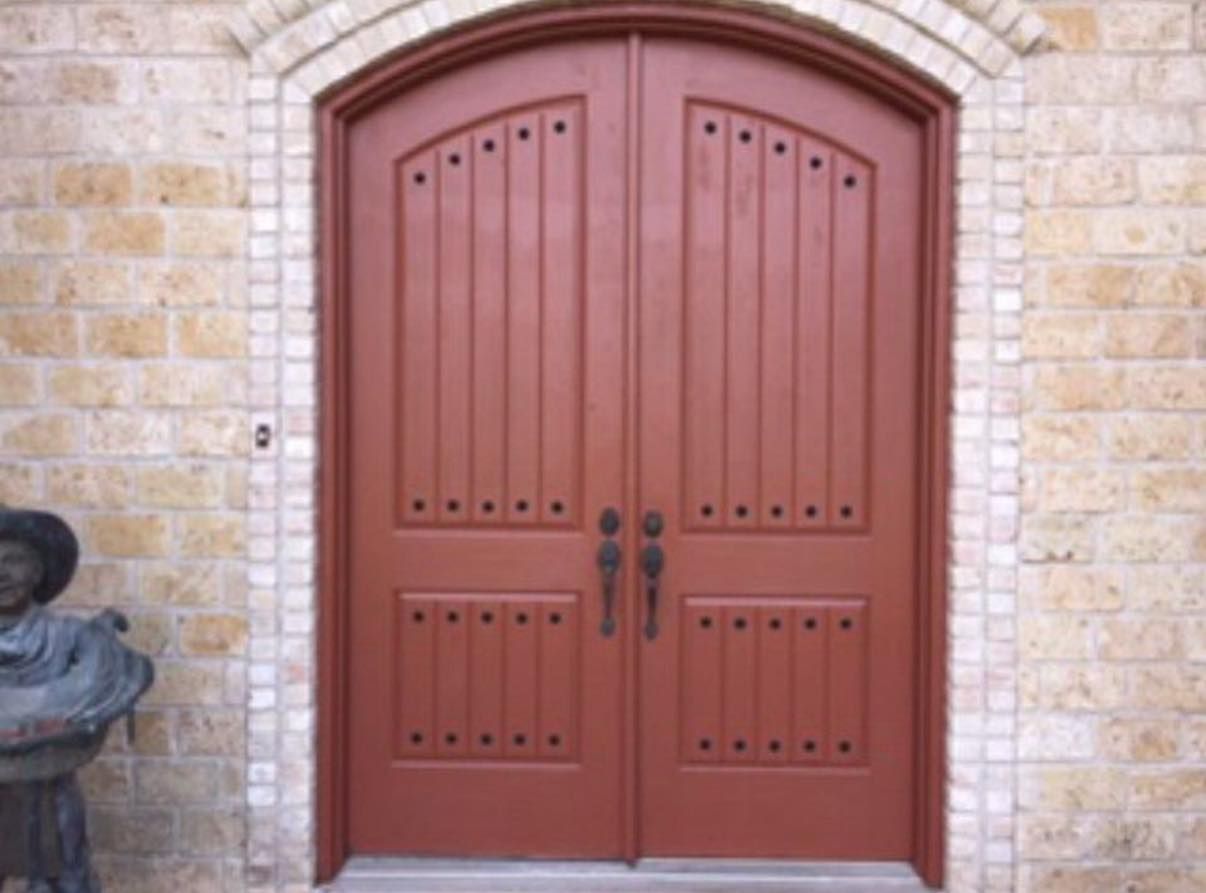 Wooden double doors with iron handles set in a stone wall, with a small statue at the left edge