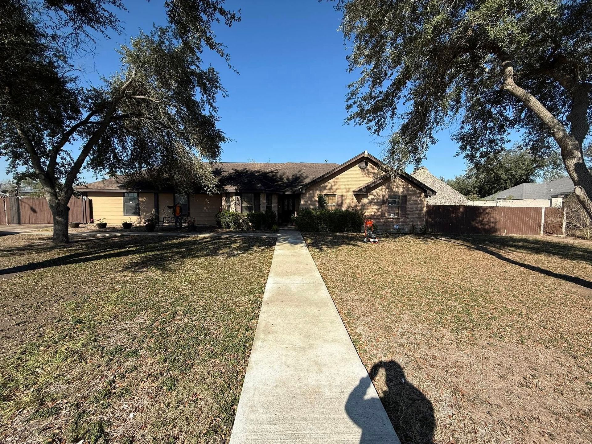 Single-story house with a front walkway, trees, and a shadow on the lawn under a clear blue sky