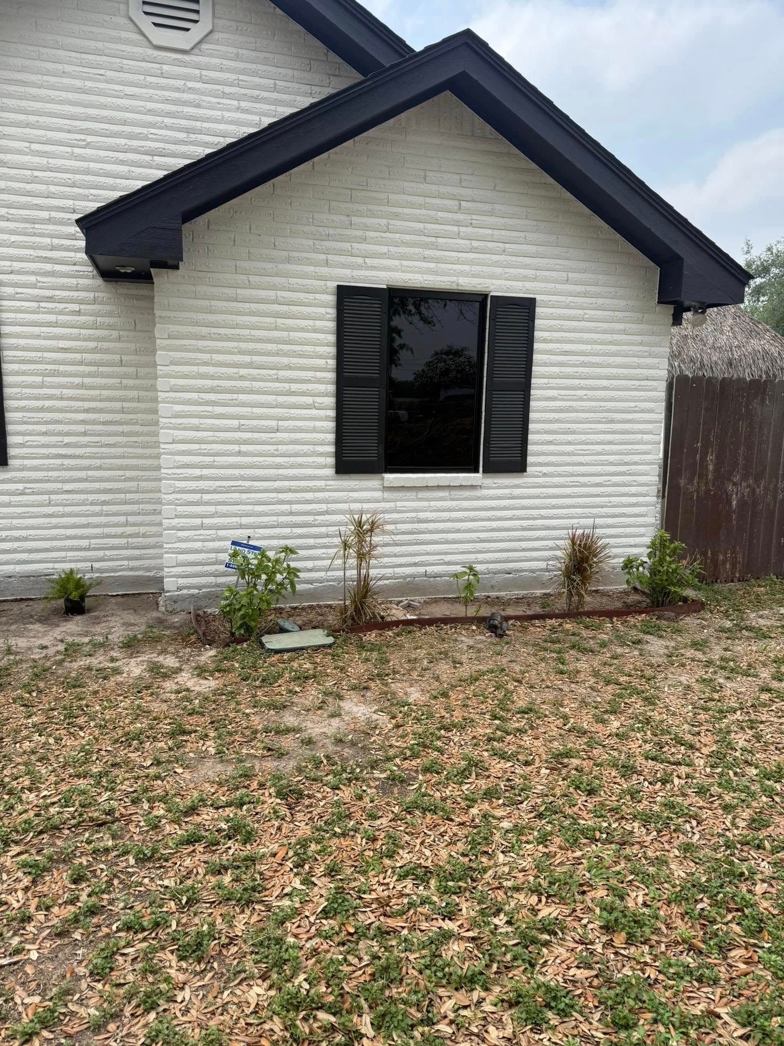 Front exterior of a house with white siding, dark trim, and a small lawn with shrubs.
