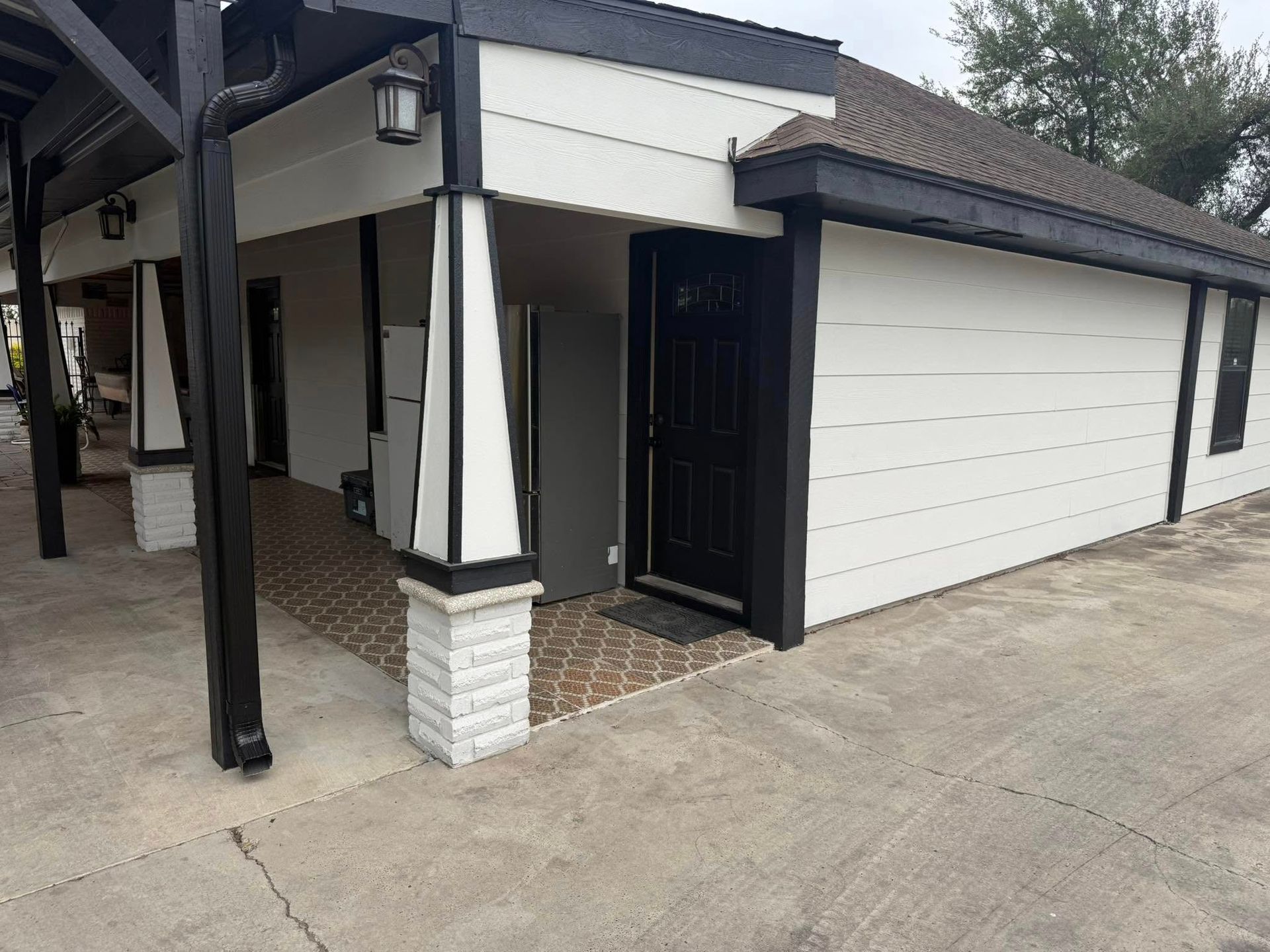 Covered porch and driveway beside a white garage door on a house exterior