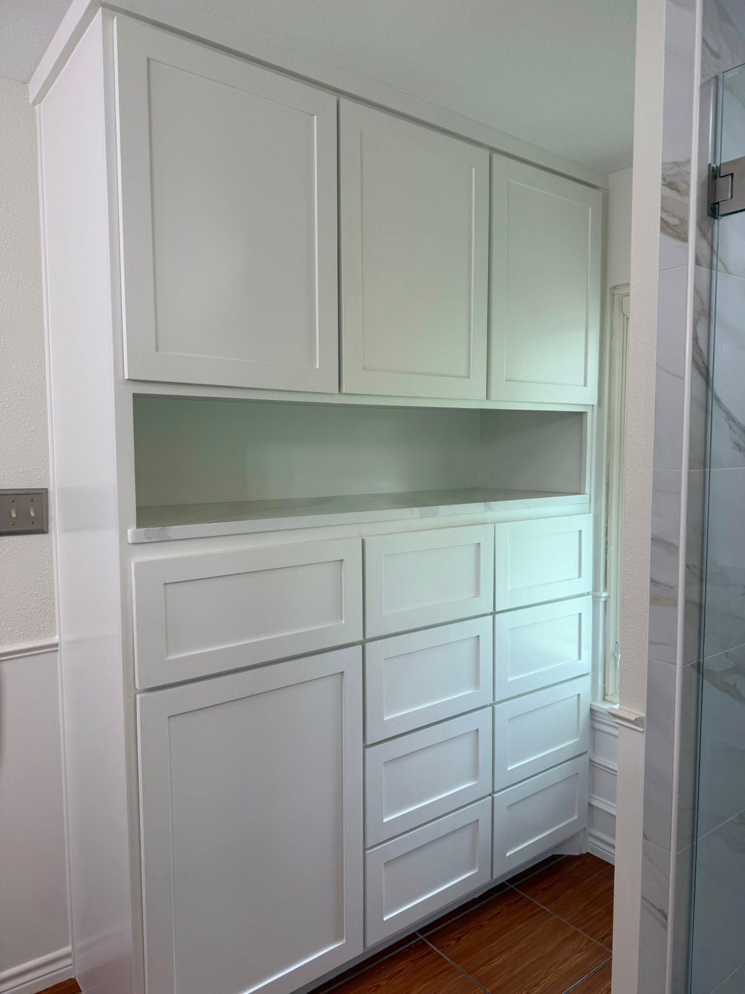 Built-in white cabinets with a central open shelf in a narrow hallway or alcove.