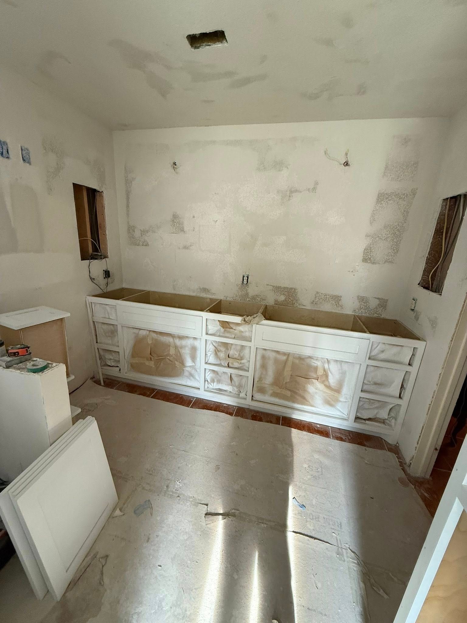 Small unfinished kitchen with white cabinets, worn walls, and a sink under renovation.