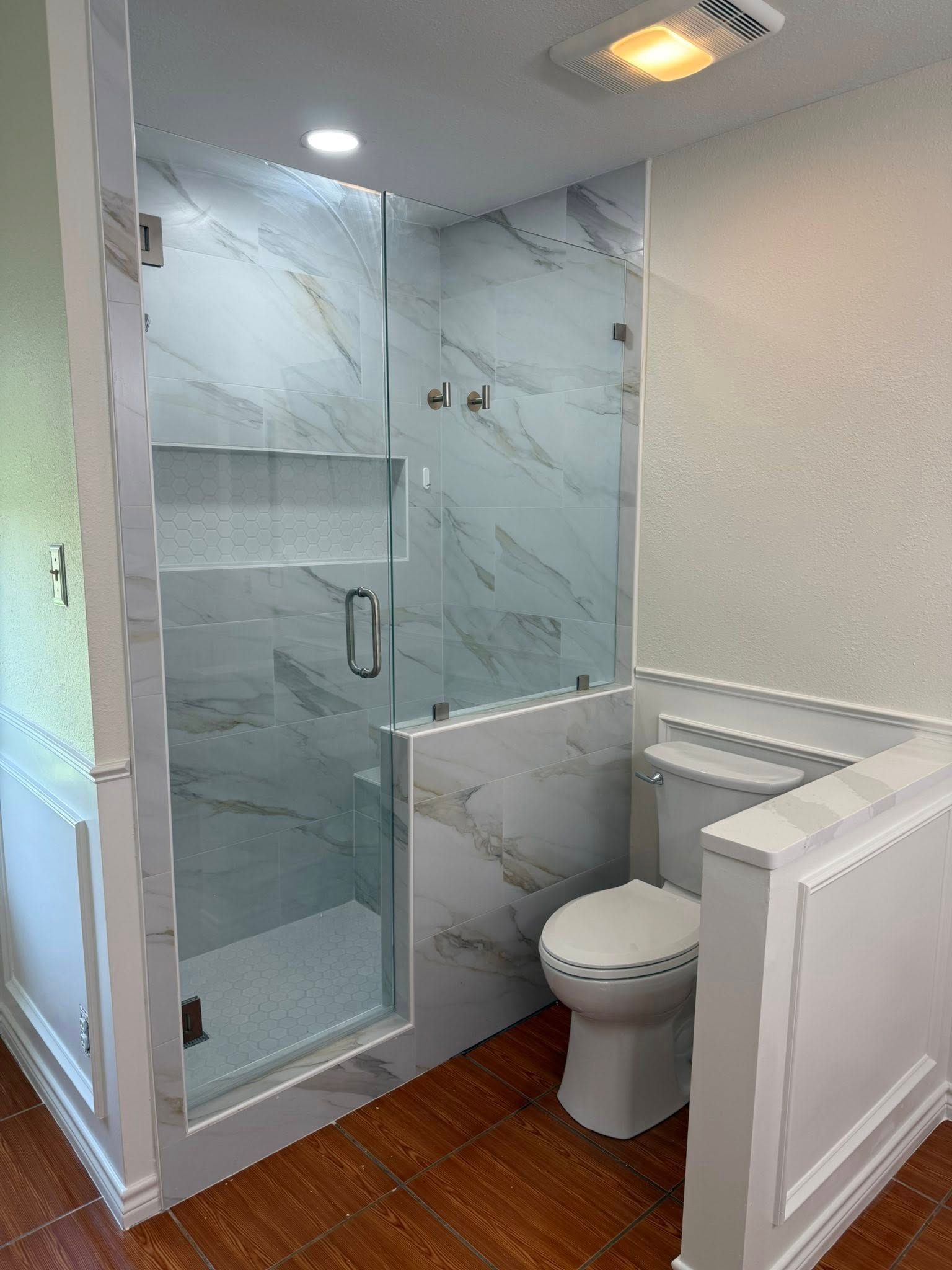 Small bathroom with a glass shower, toilet, and white vanity in marble and wood finishes