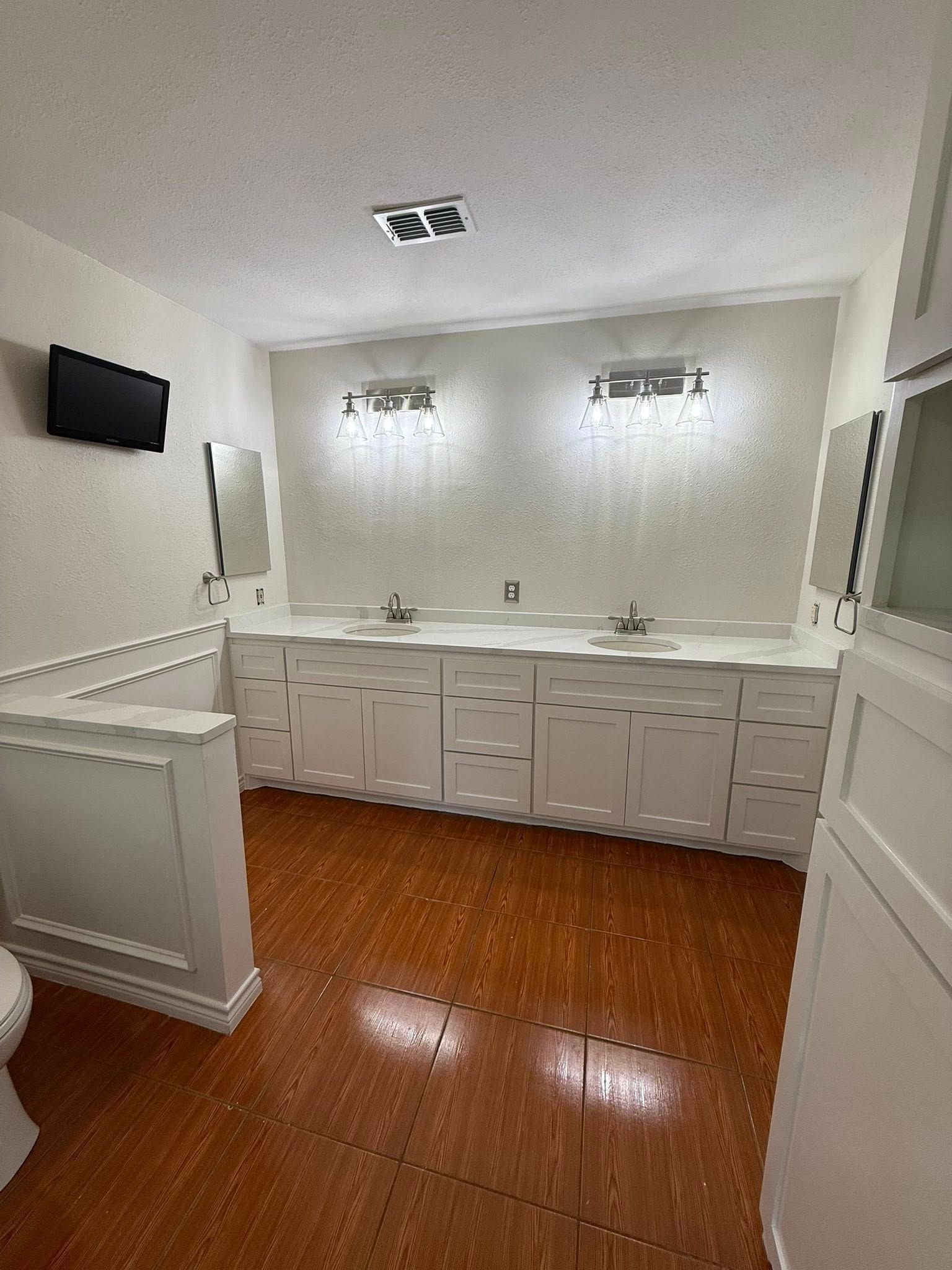 Spacious bathroom with double vanity, mirrors, wall lights, white walls, and wood-look tile floor