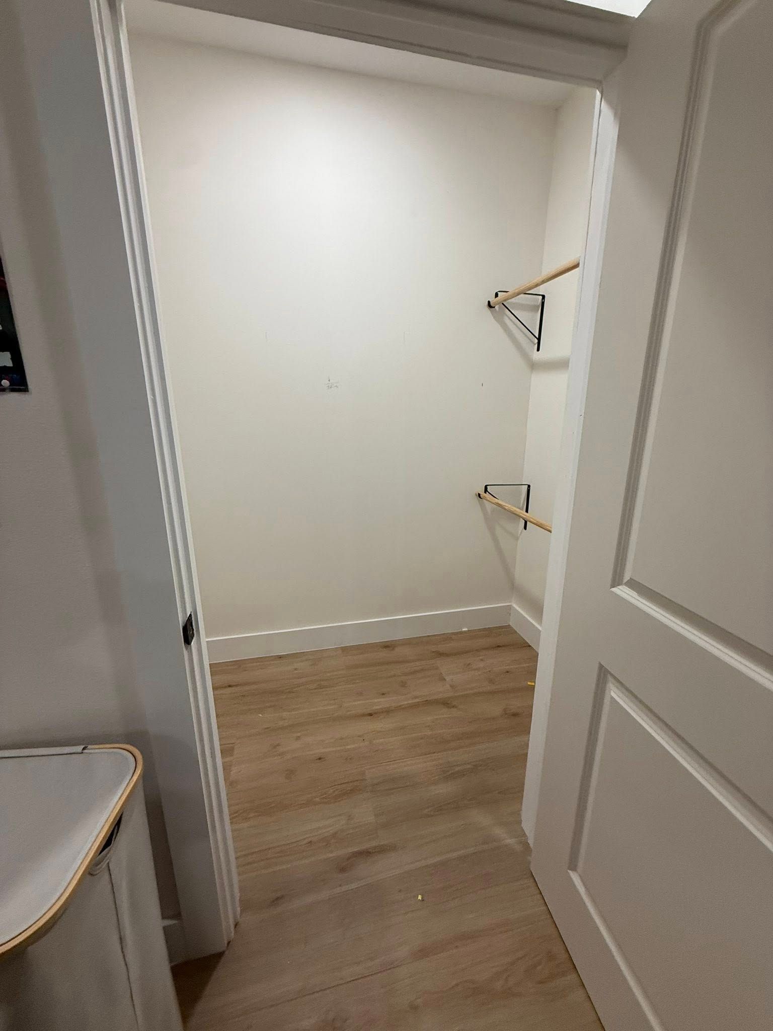 Open closet with white walls, wood flooring, and built-in hanging shelves.