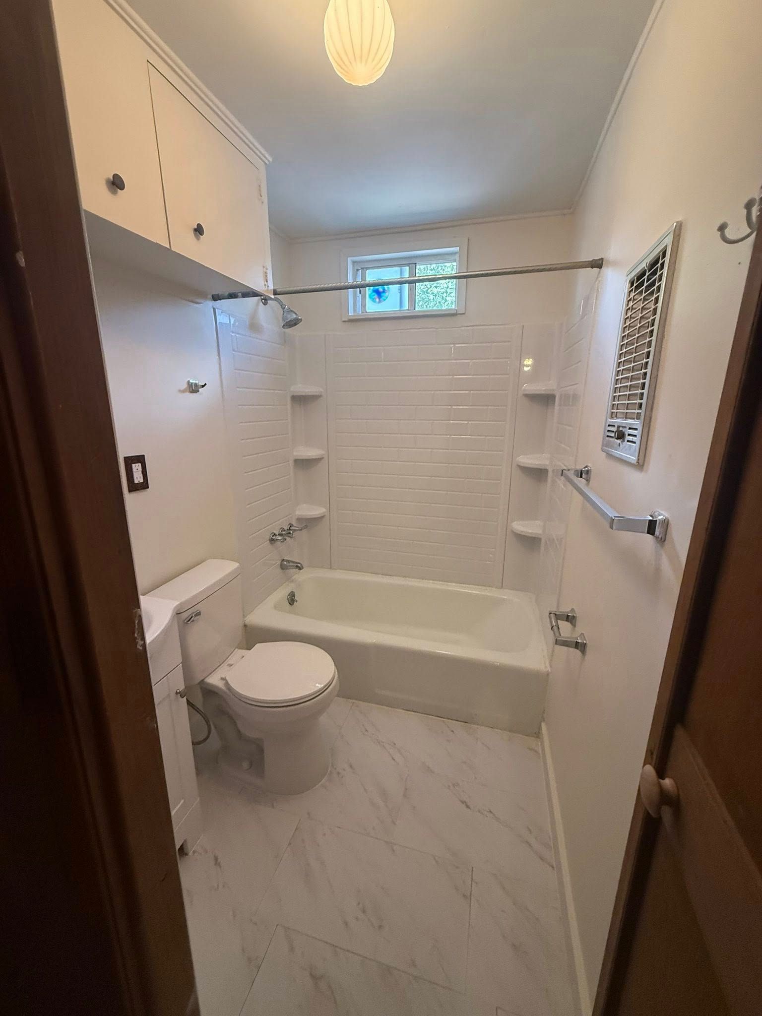 Small bathroom with tub-shower, toilet, vanity cabinet, white tile, and a small frosted window.