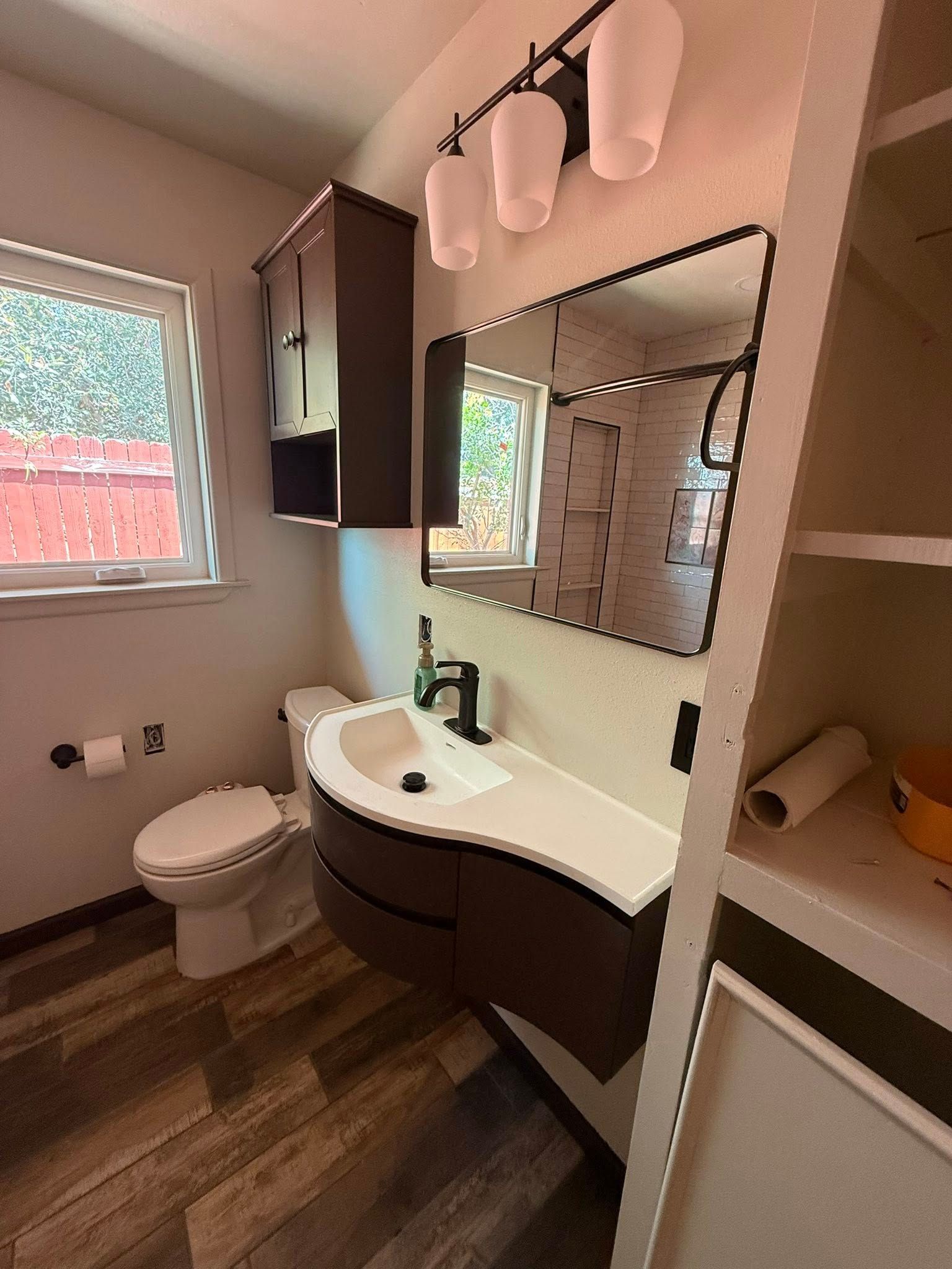 Small bathroom with a white vanity, mirror, toilet, window, and dark wood cabinets.