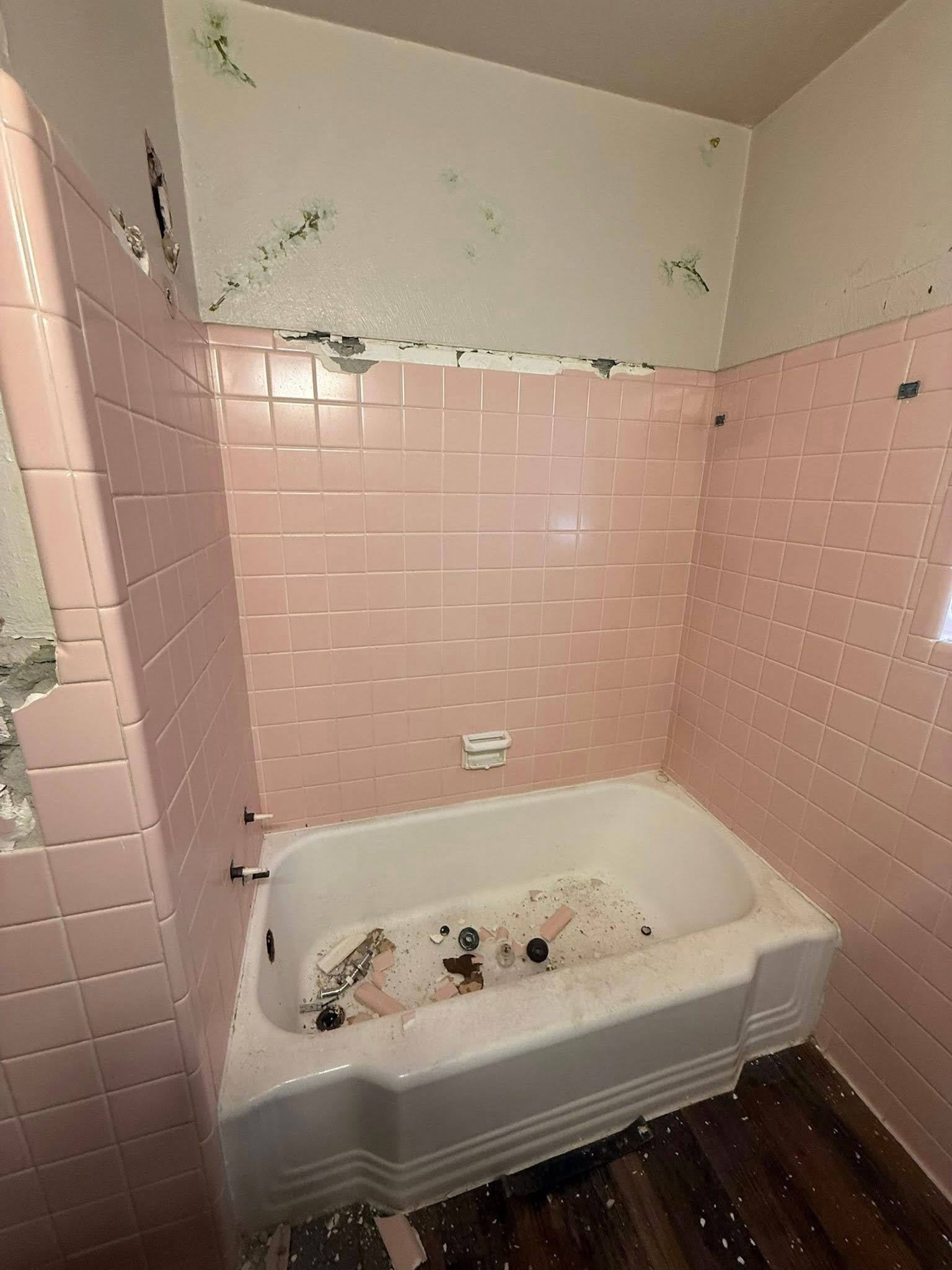 Damaged pink-tiled bathroom with a bathtub filled with debris and stained walls near the ceiling