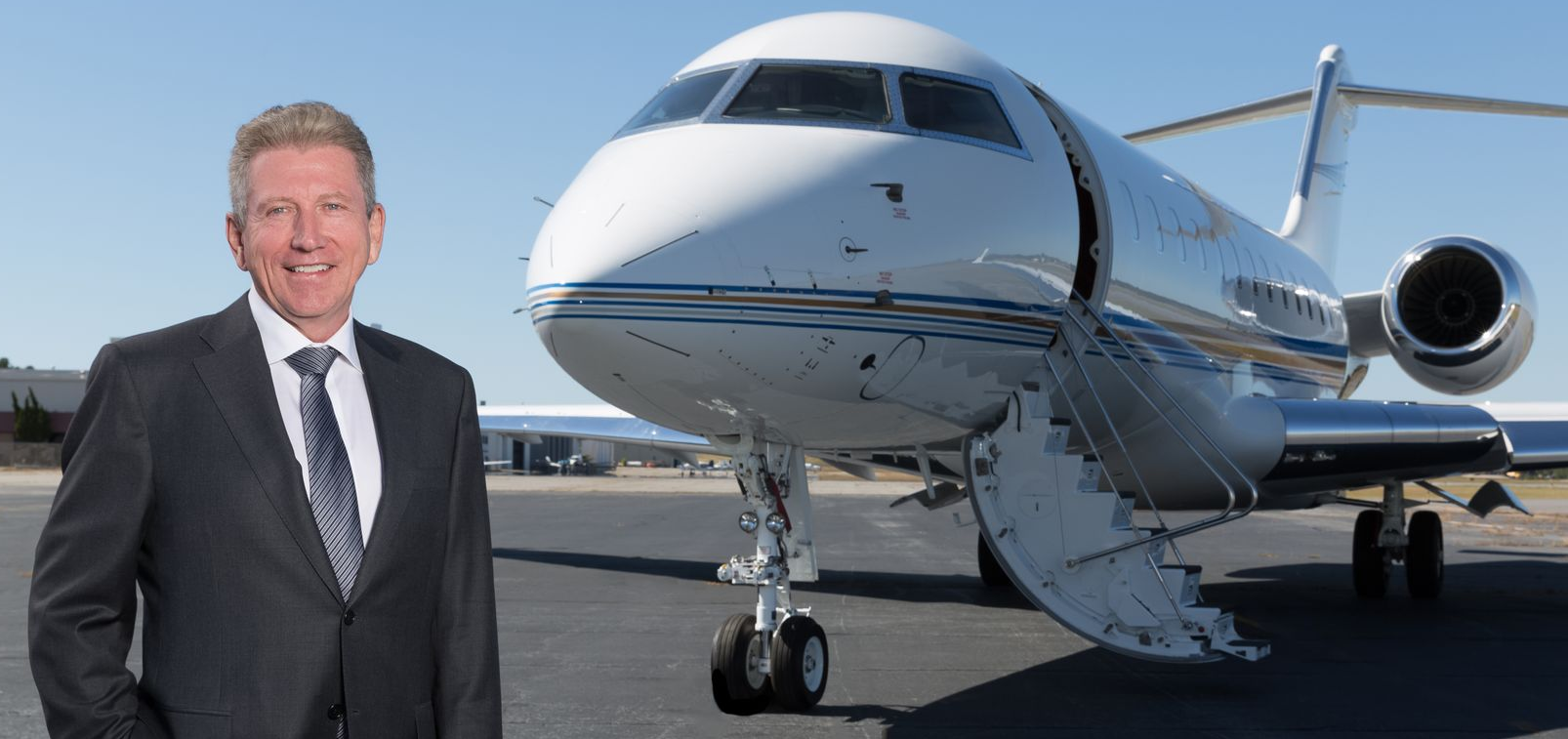 Scott Rogers at Amjet Aviation; Man in suit stands beside a private jet on a tarmac.