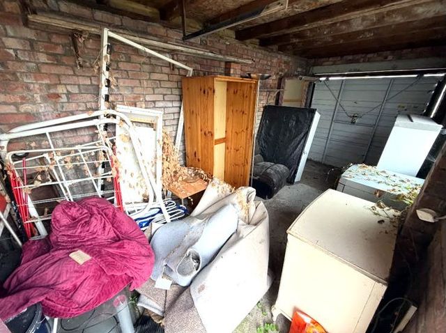 Garage in Penarth before clearance, filled with bed frames, a pine wardrobe, an armchair, rolled carpet and white goods