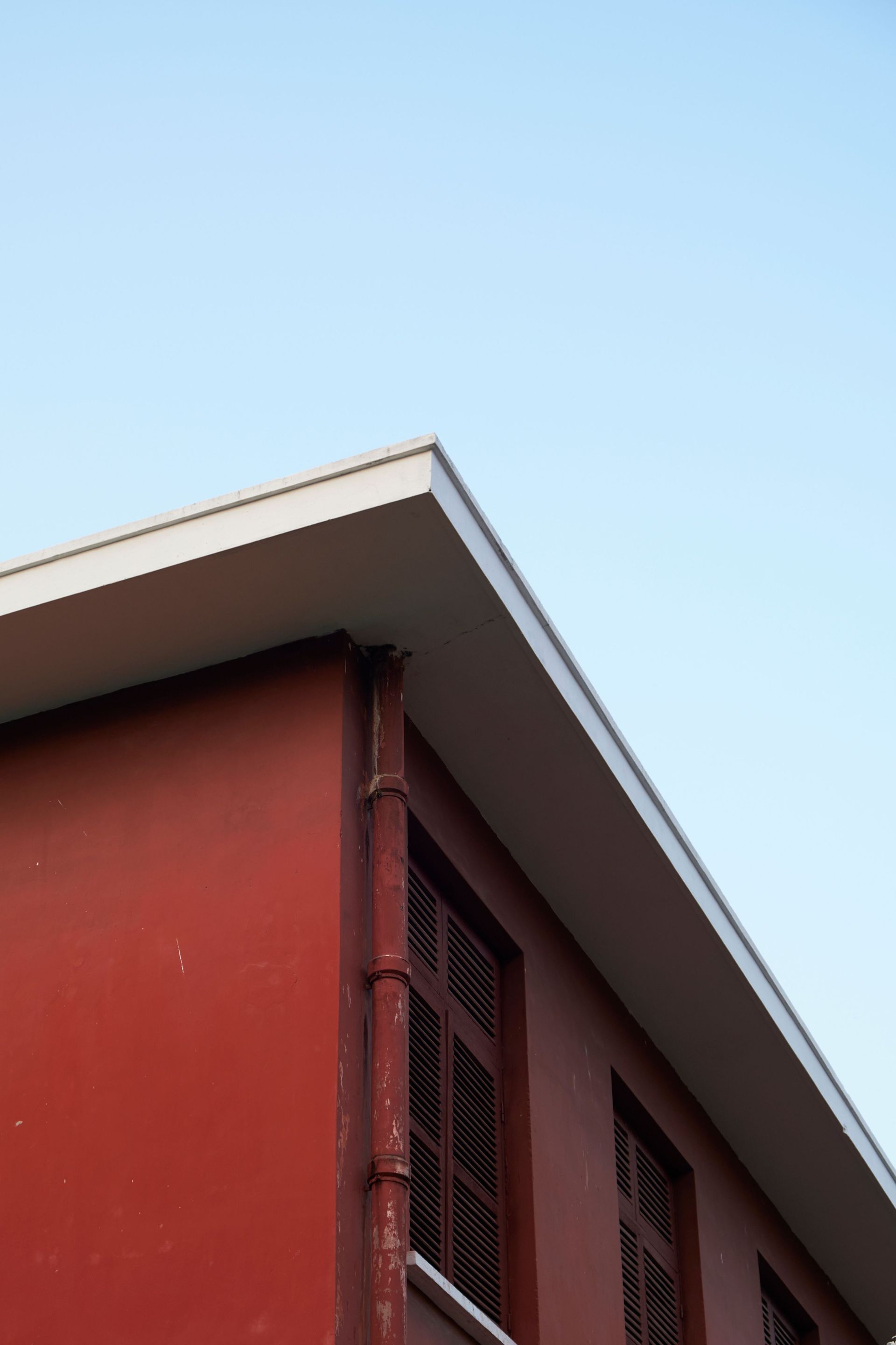 Red building corner with white roof trim against a clear blue sky
