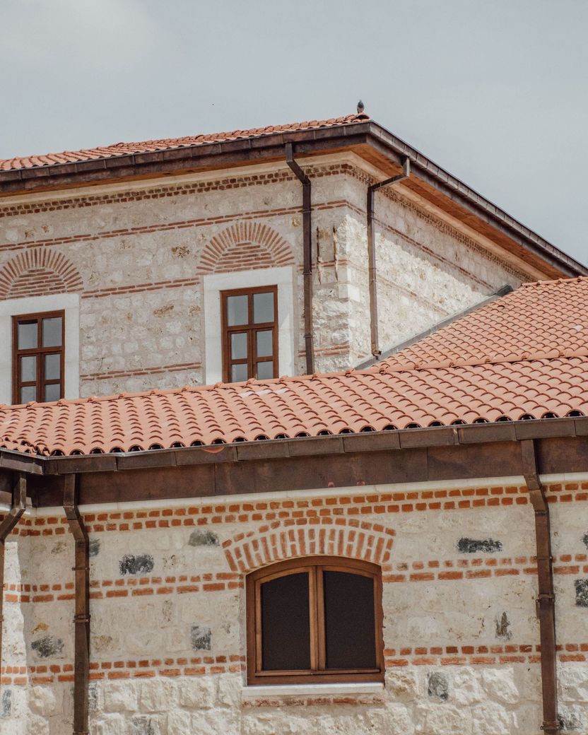 Brick building with red tile roof, white patterned facade, and brown-framed windows under a gray sky