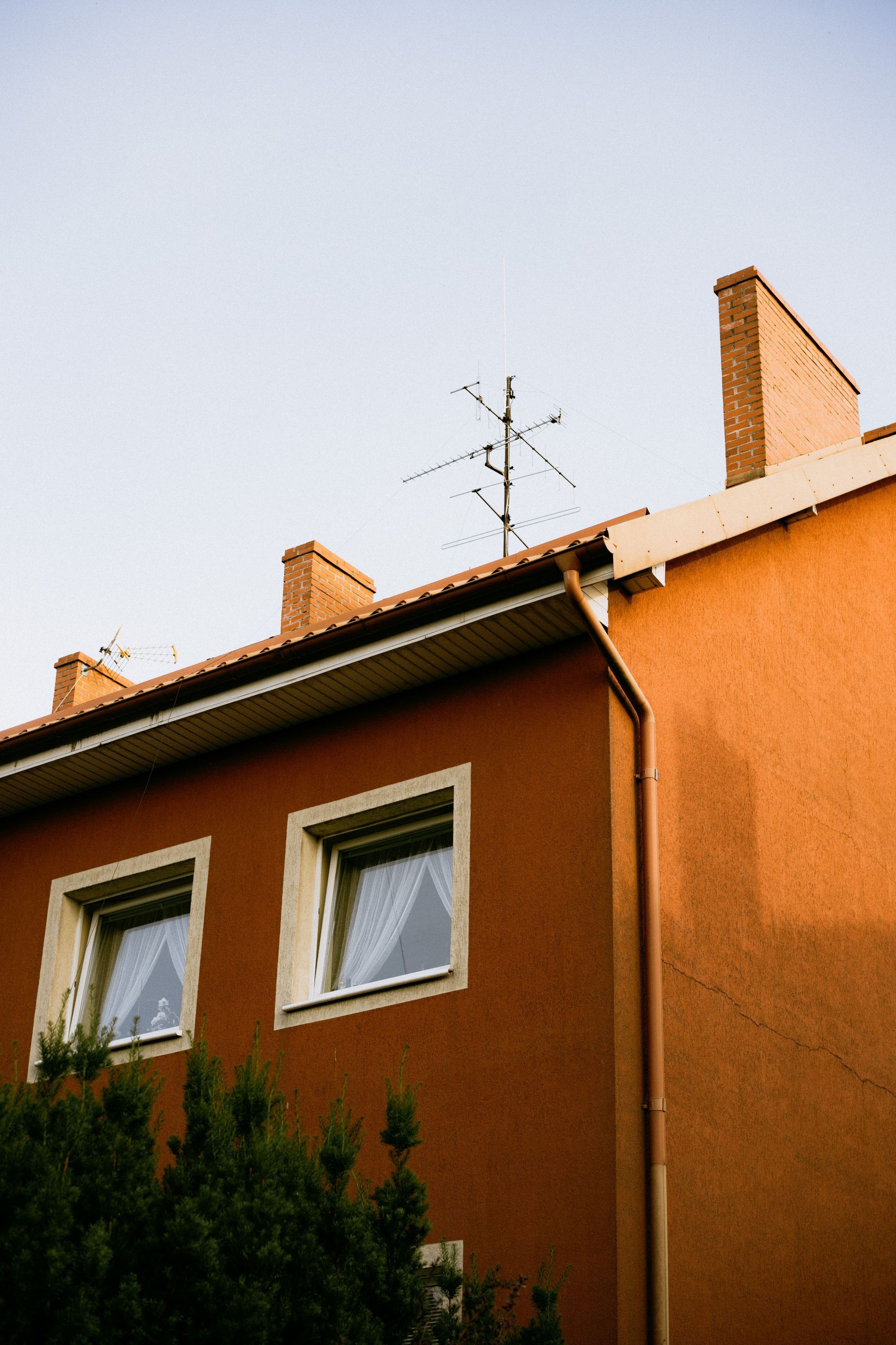 Orange house facade with two windows and rooftop antennas against a blue sky