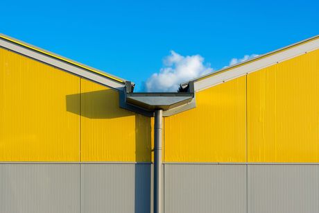 Yellow industrial building with a central downspout against a blue sky and clouds