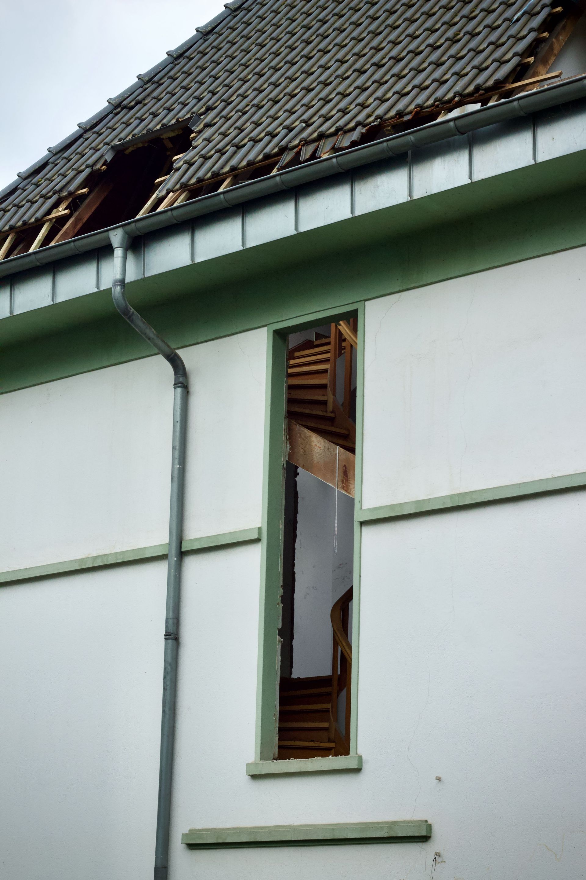 Damaged house wall with a broken window under a tiled roof