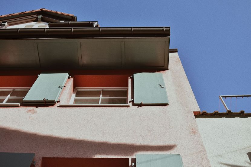 Low-angle view of a white house with teal shutters against a clear blue sky