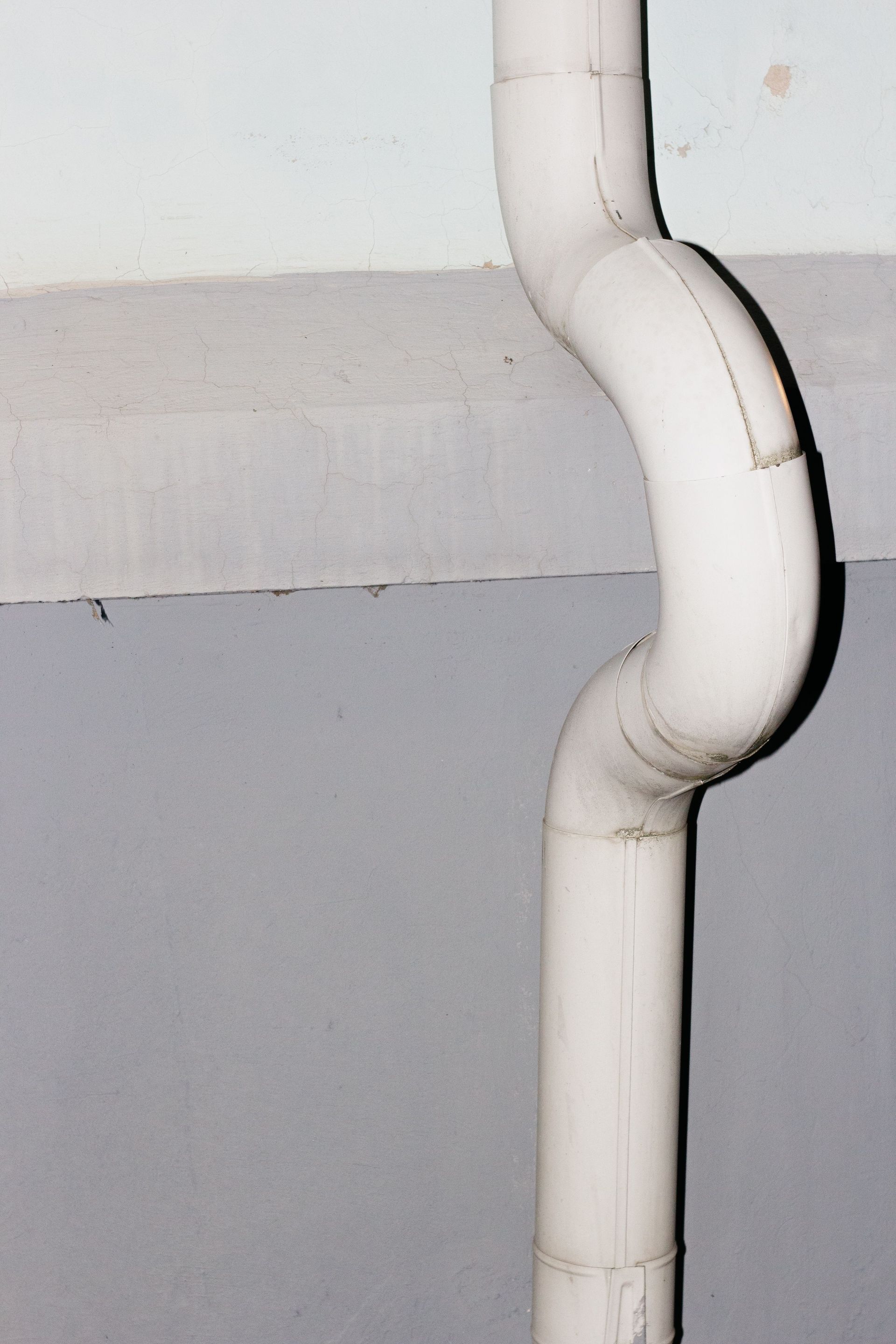 White PVC pipe with a curved bend mounted against a light gray wall.