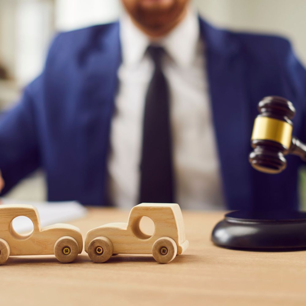 Wooden toy cars and gavel on desk, man in suit in background.