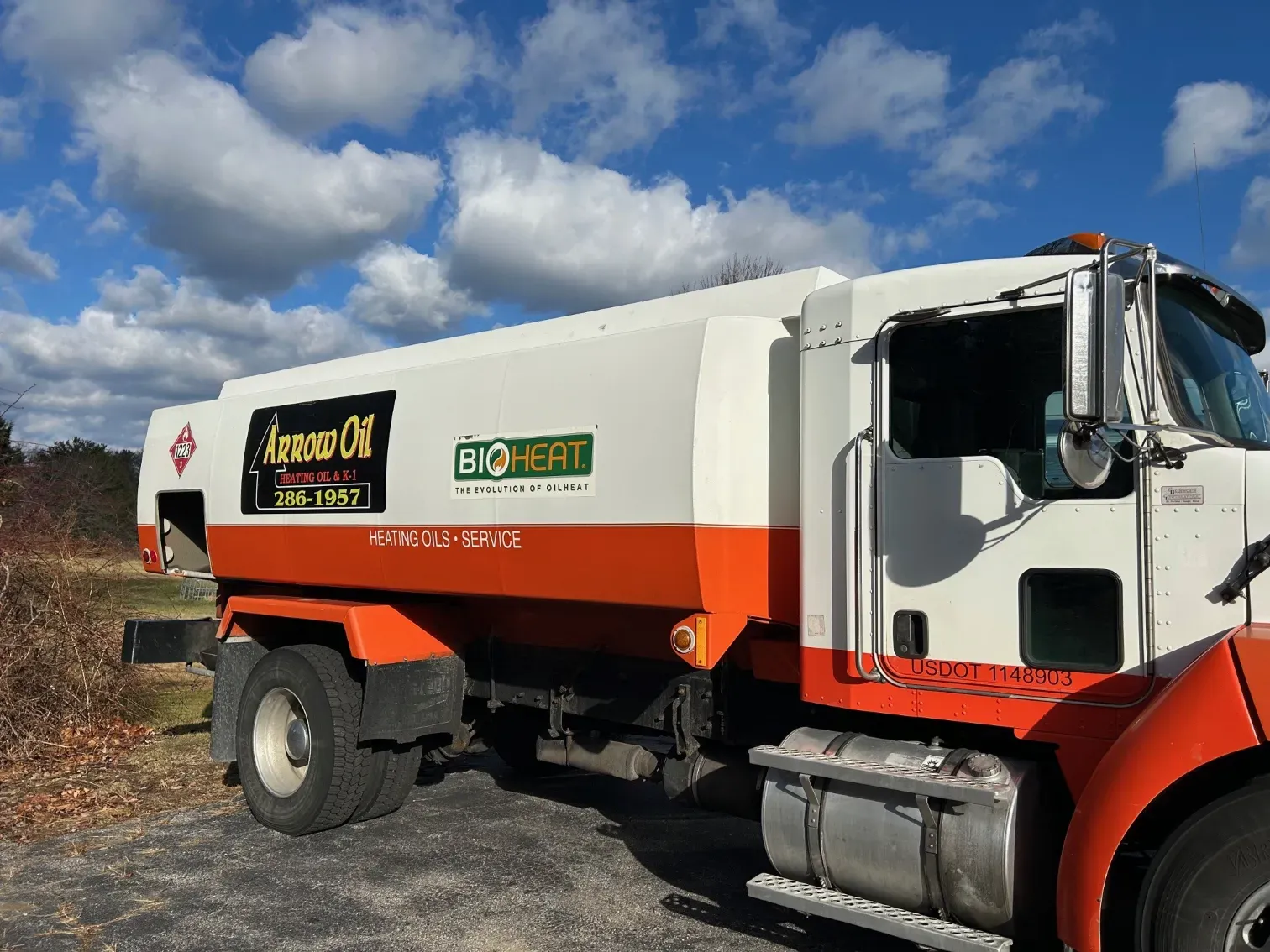 A white and orange tanker truck is parked on the side of the road.