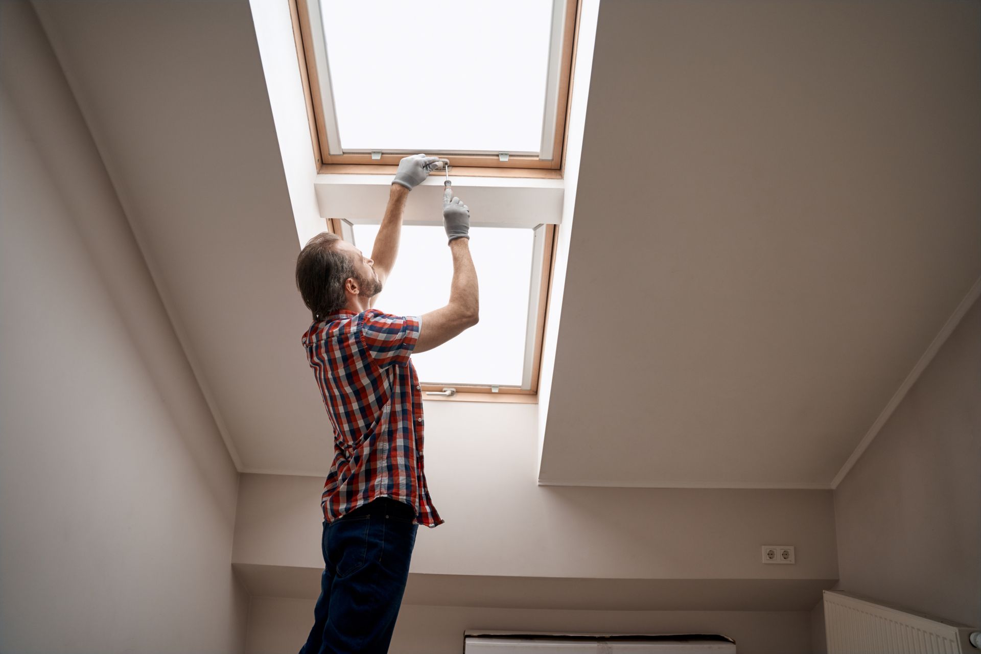 A repairman is maintaining a handle on a skylight window with a screwdriver. A repairman is maintaining a handle on a skylight window with a screwdriver.