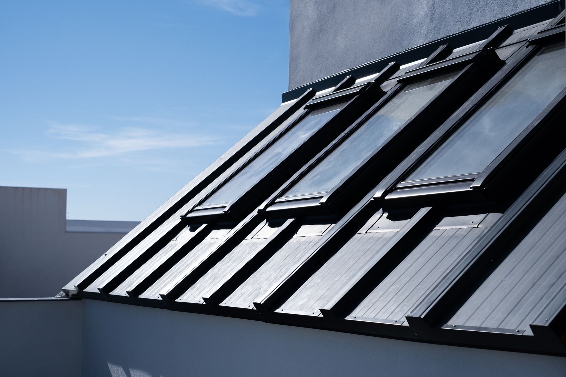 Slanted roof with several skylights beneath a clear blue sky.