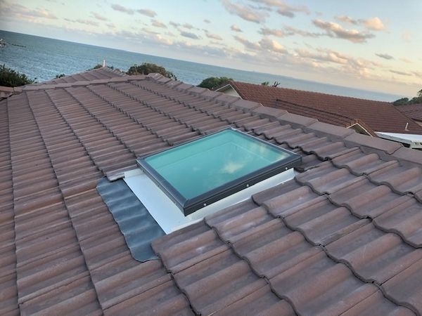 Skylight on a tiled roof with ocean view in background.