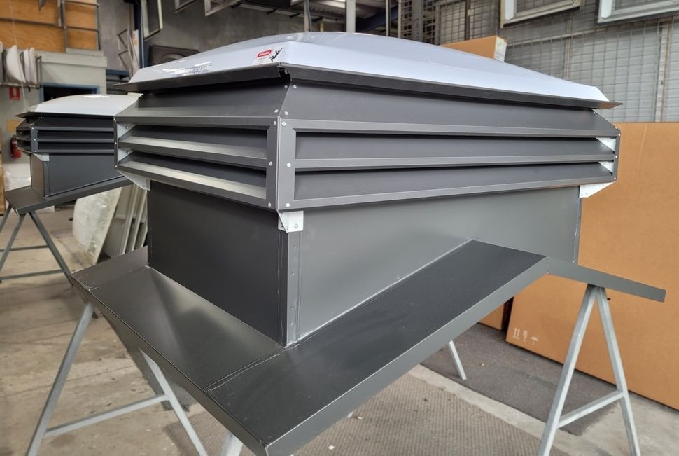 Two gray industrial ventilation units, with layered louvers, sitting on sawhorses.