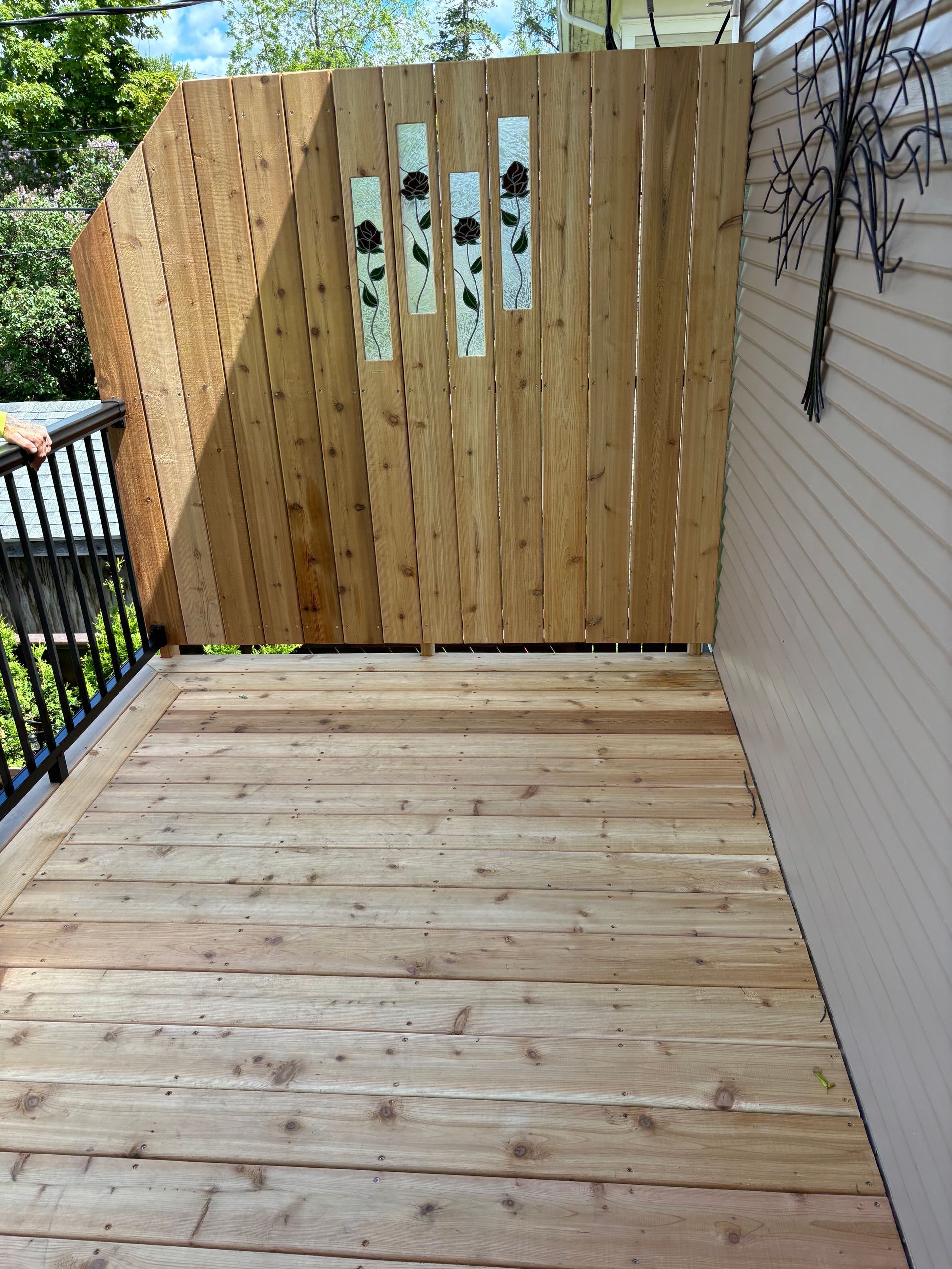 Wooden deck with cedar fence, decorated with floral art. Beige siding to the right.