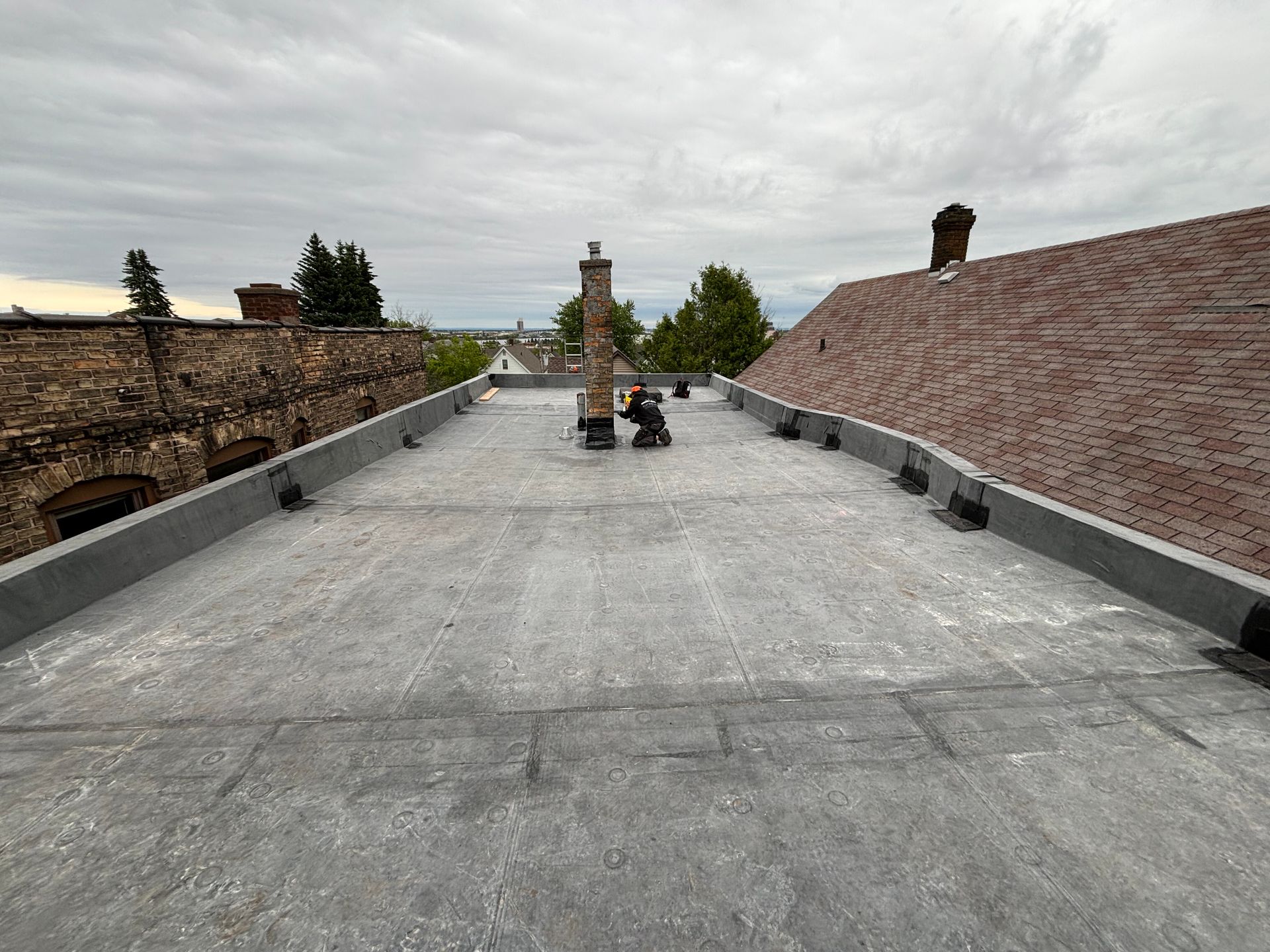 Flat, gray rooftop with a central chimney and cityscape background under an overcast sky.