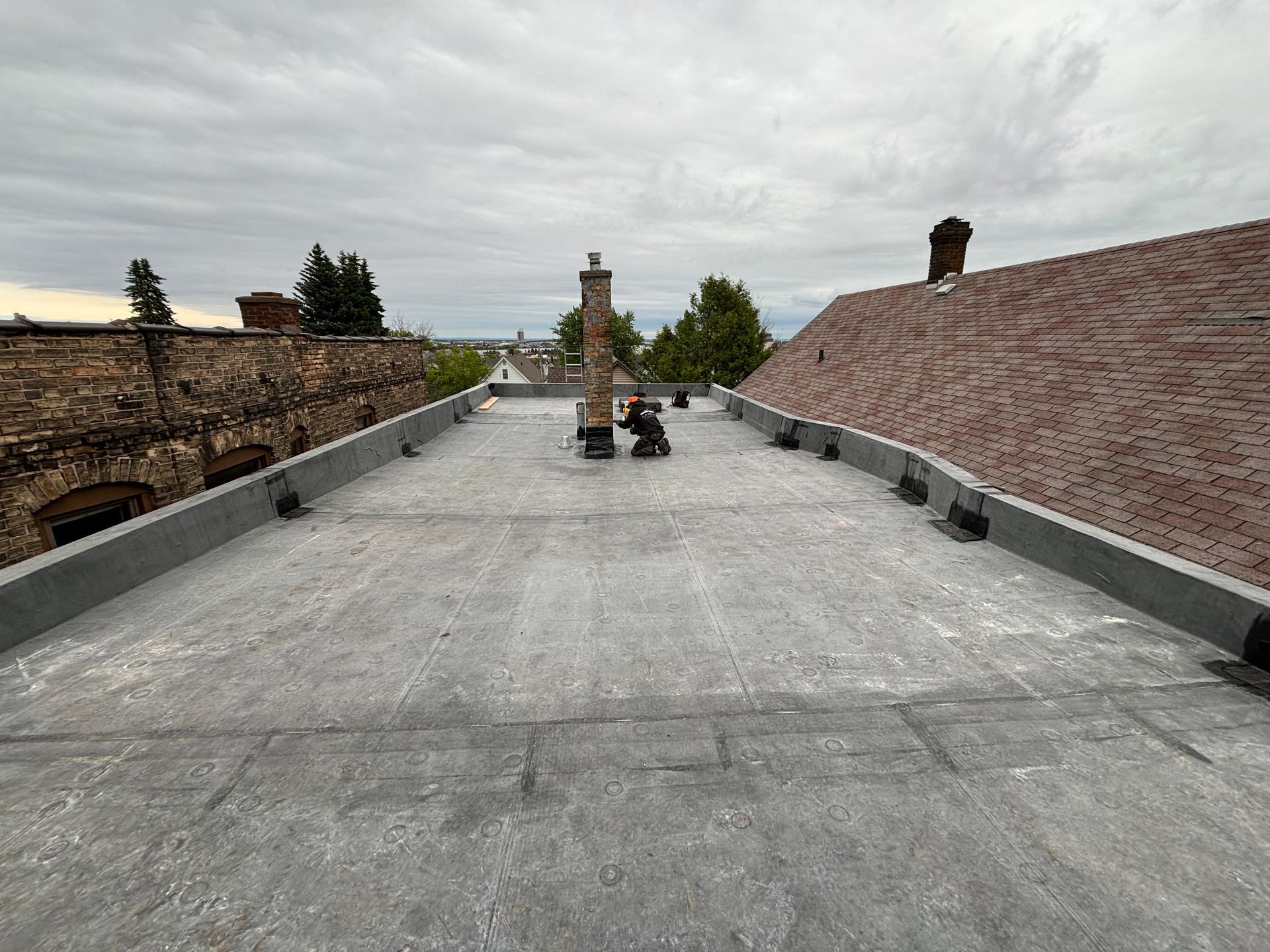 Flat, gray rooftop with a brick chimney and person working. Cloudy sky background.
