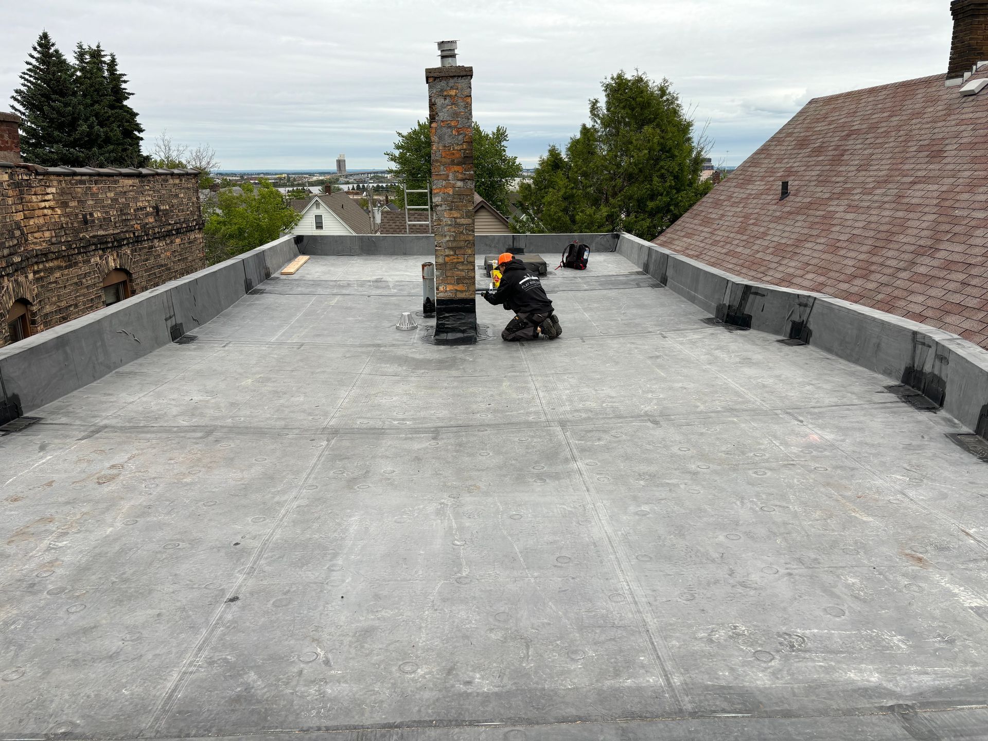 Workers on a flat roof around a brick chimney, cloudy sky background.