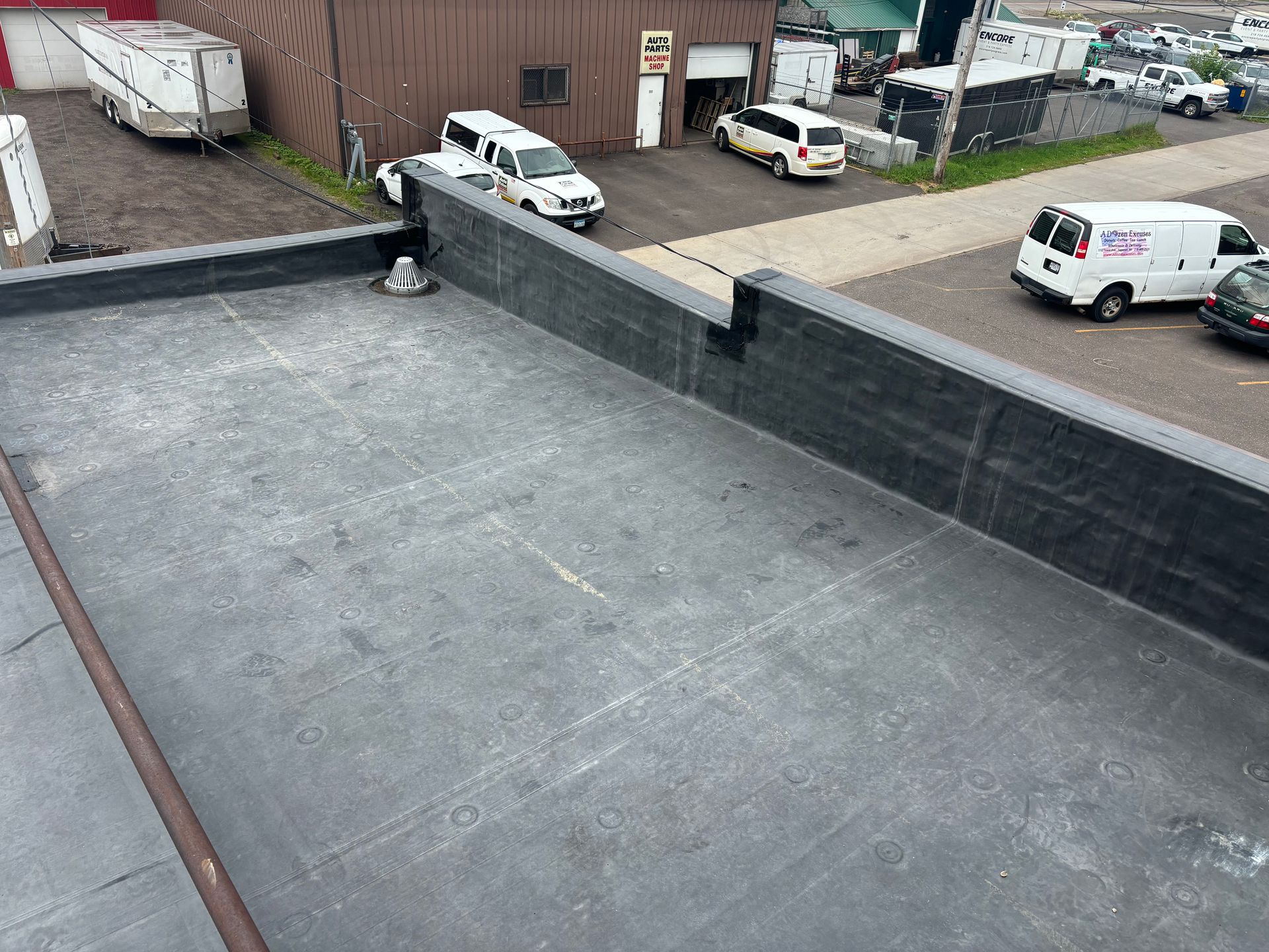 Black flat roof with building and vehicles in the background.