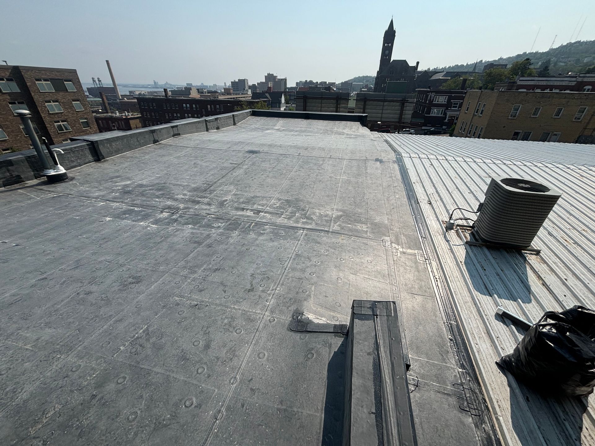 Rooftop view of urban buildings and a distant church steeple under a clear sky.