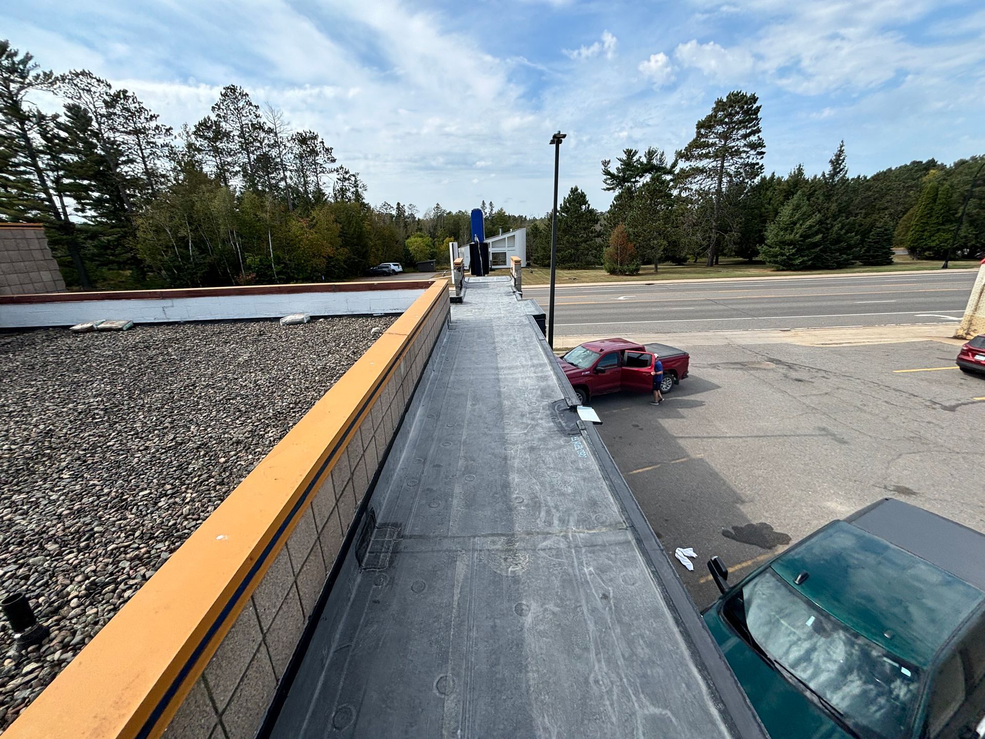Rooftop view of a building with a black surface and bordering orange trim. A red truck is parked nearby.