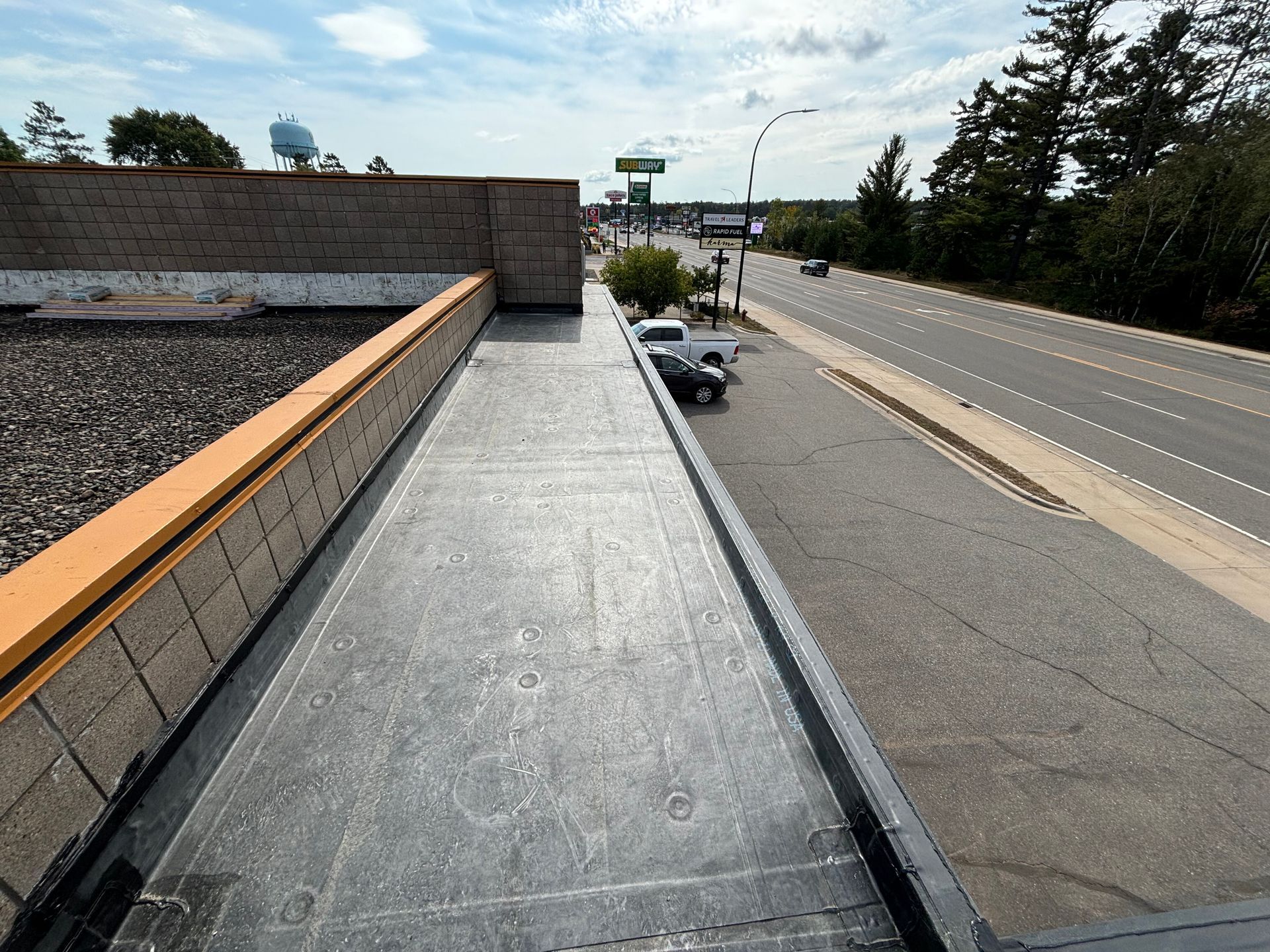 View from a flat roof overlooking a highway, a parked truck, and trees under a blue sky.