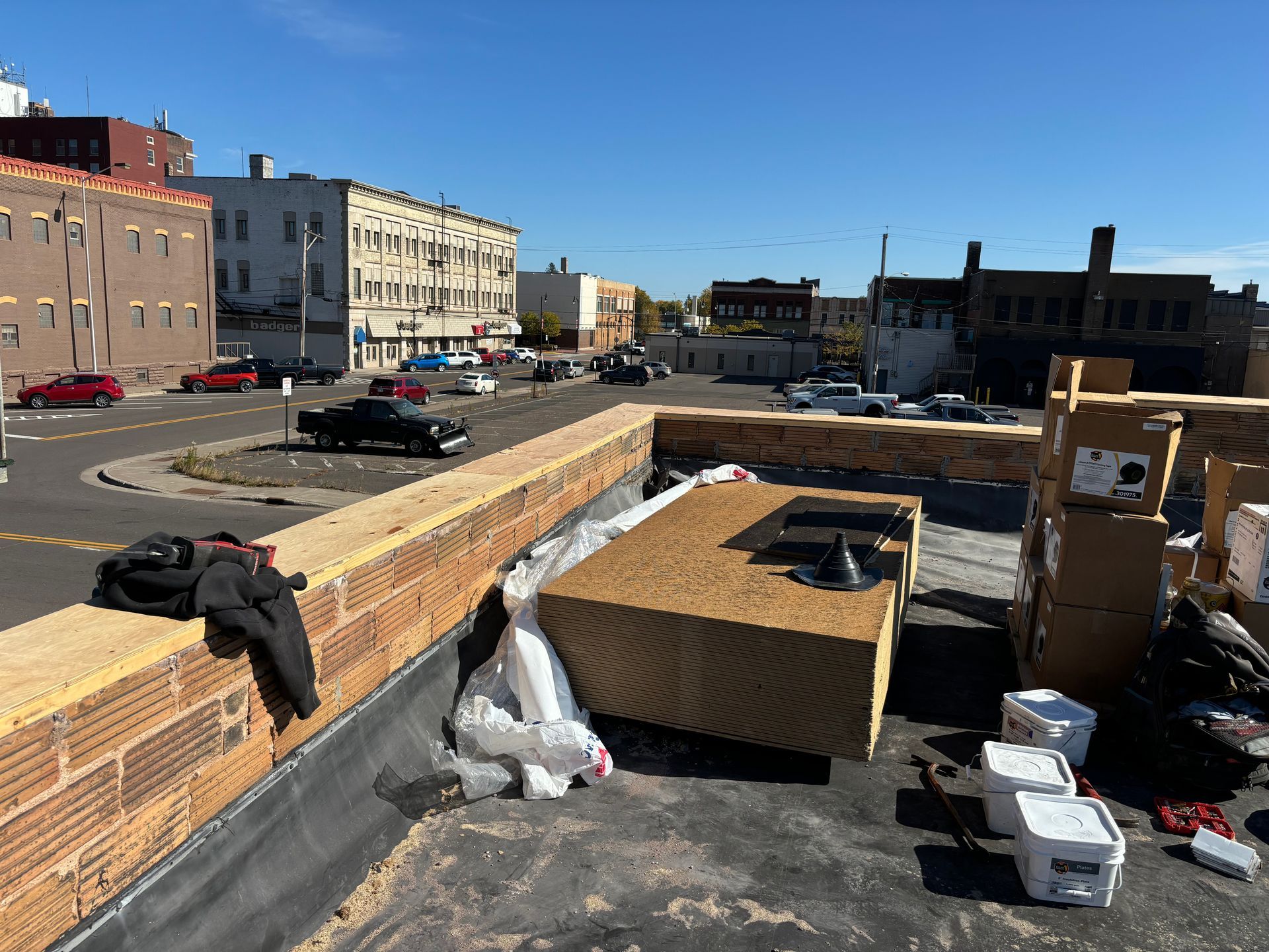 View from a rooftop: brick wall, construction materials, city street with cars, blue sky.
