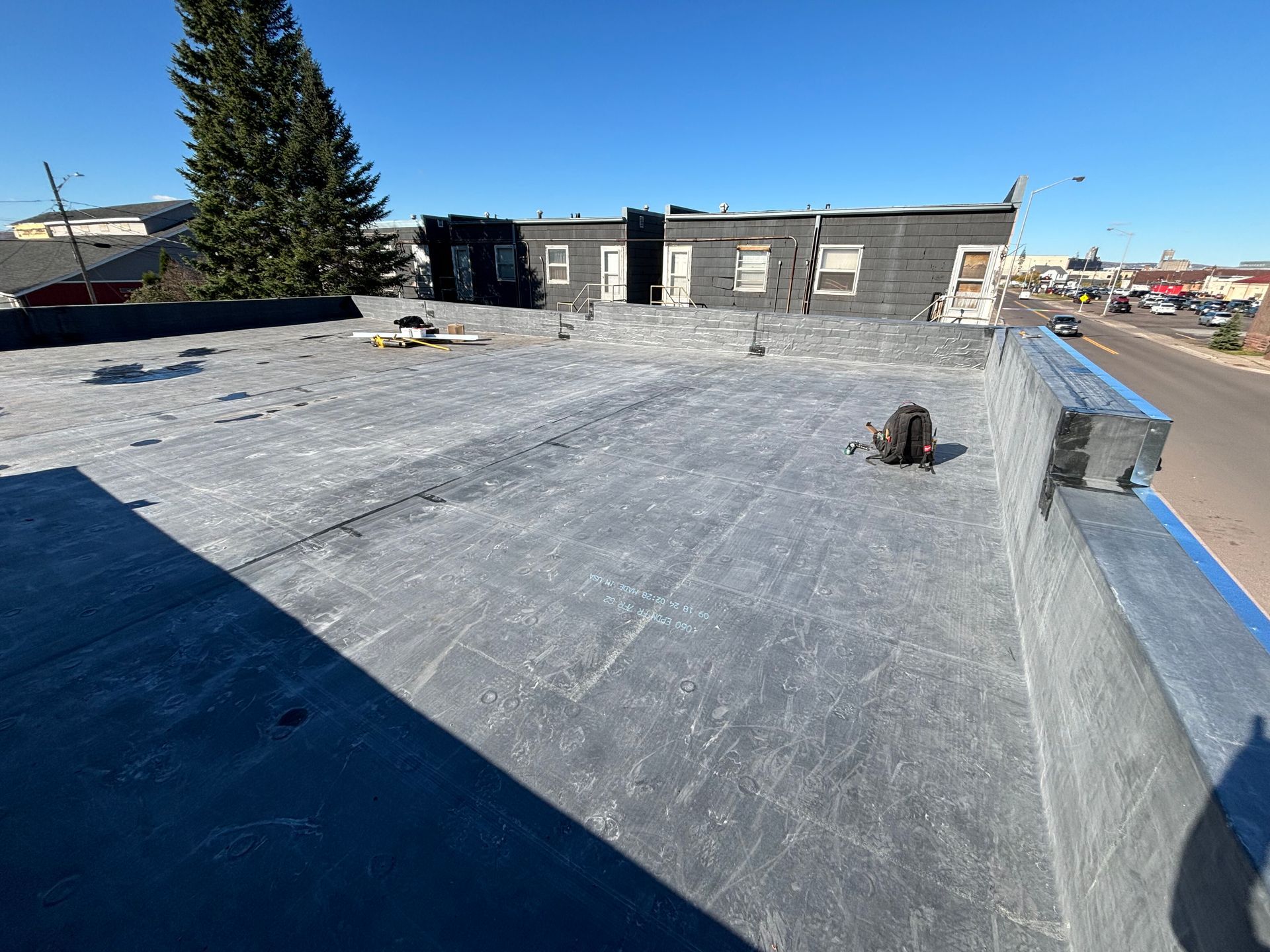 Flat, gray rooftop with a dark building in the background. The sky is blue and it’s a sunny day.