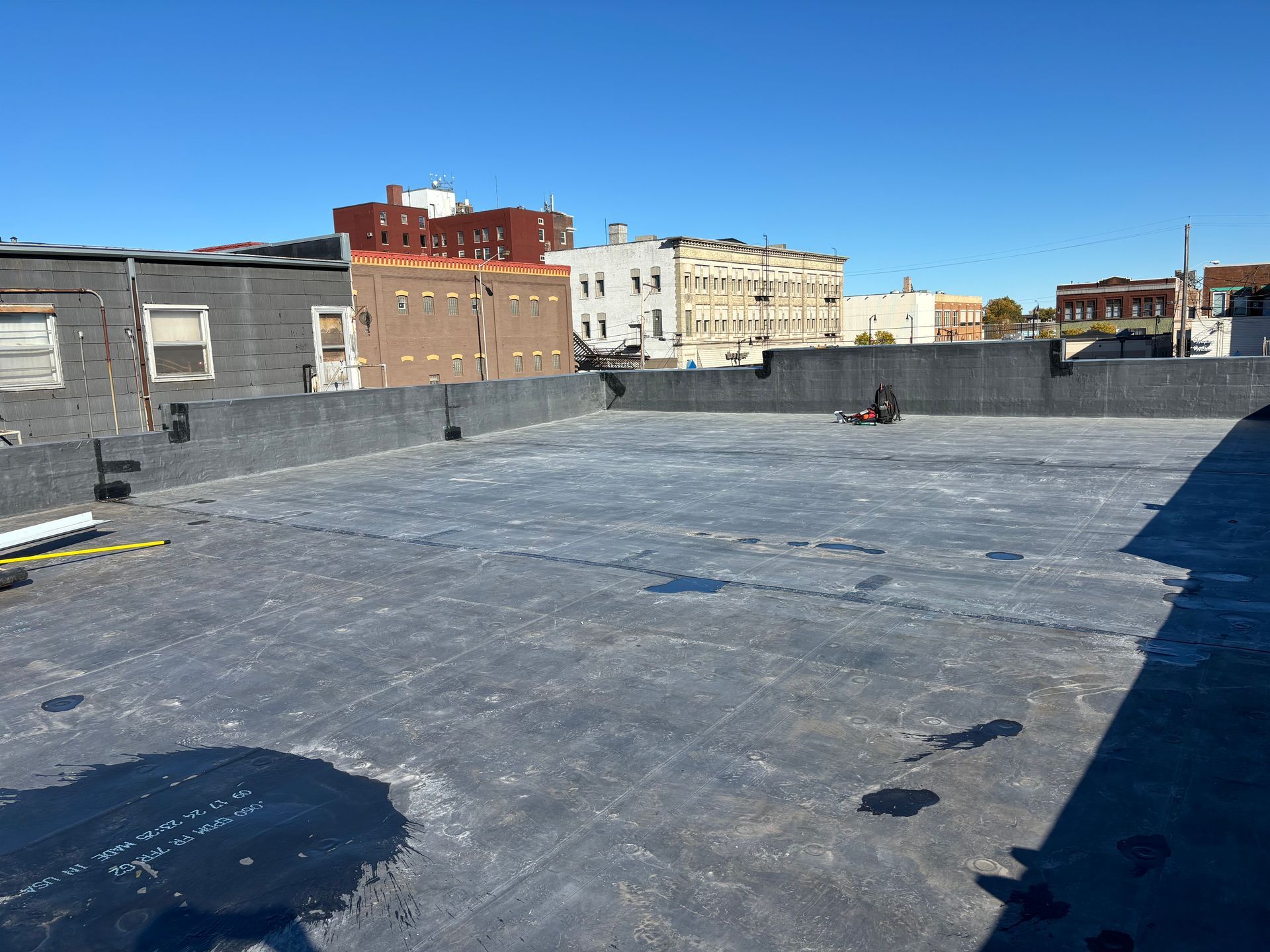 Flat, black rooftop with a cityscape backdrop on a sunny day.