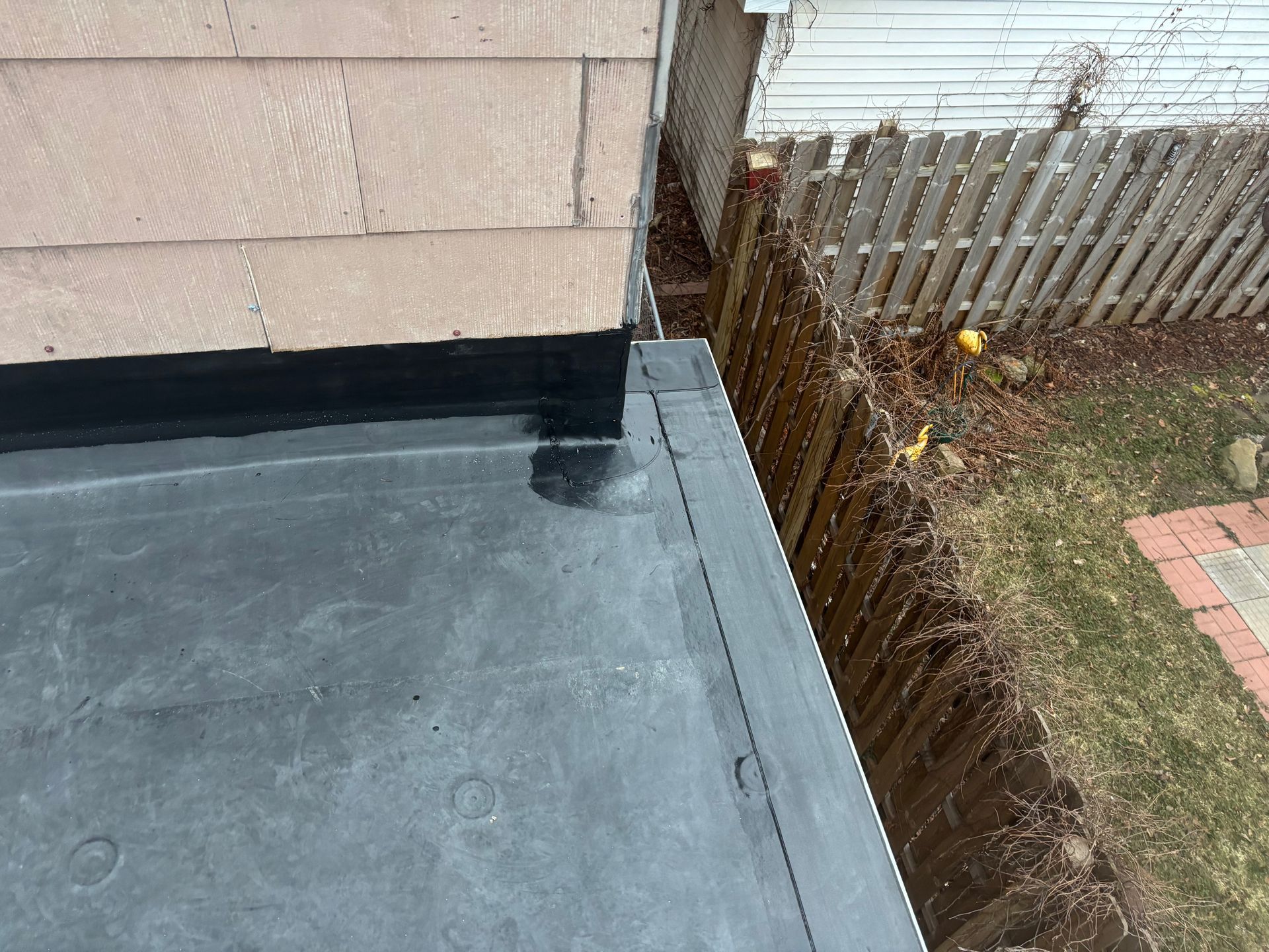 Black flat roof edge next to a wooden fence and tan siding.
