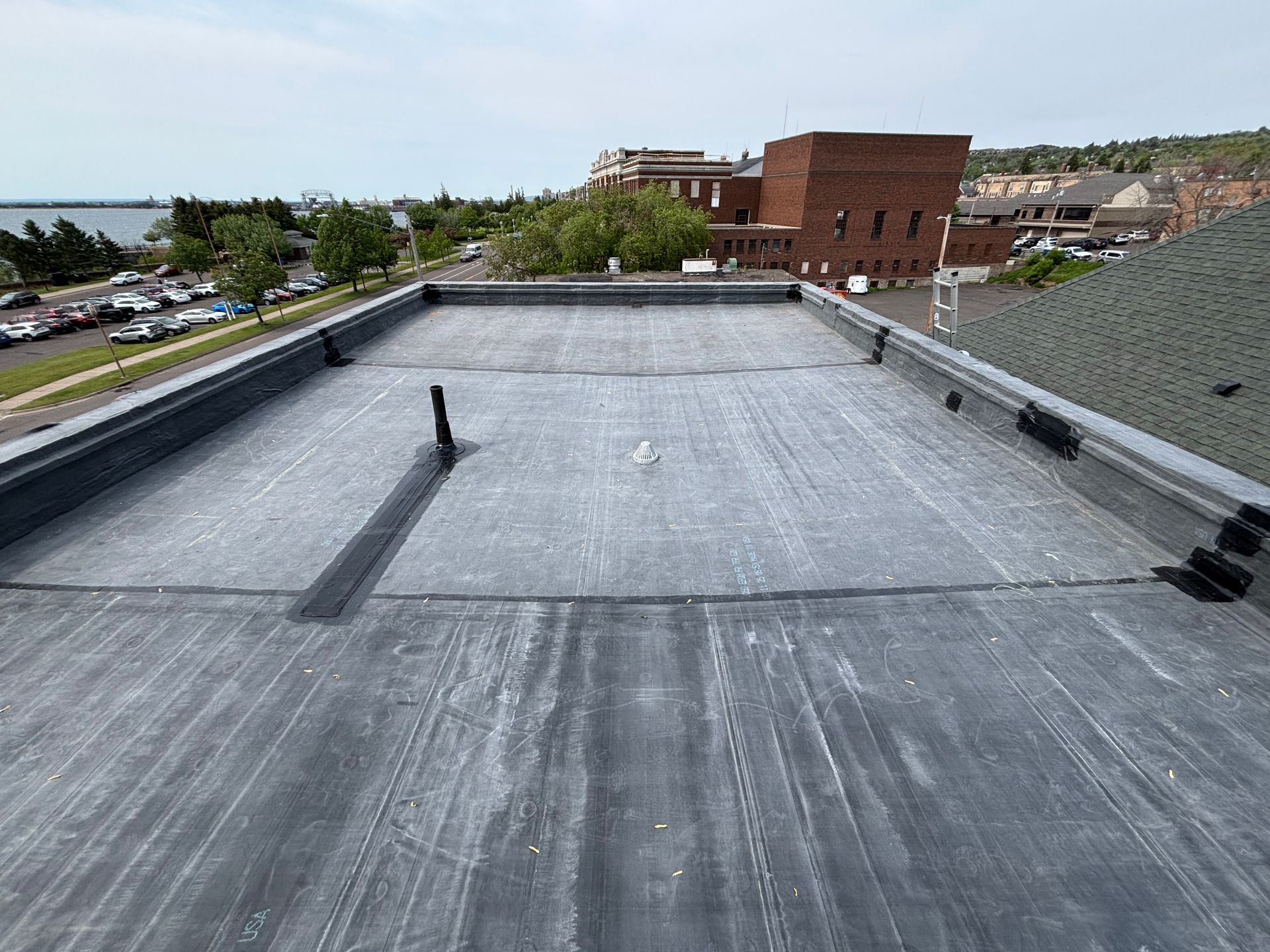 Flat, dark gray roof with light markings, near buildings and a water view.