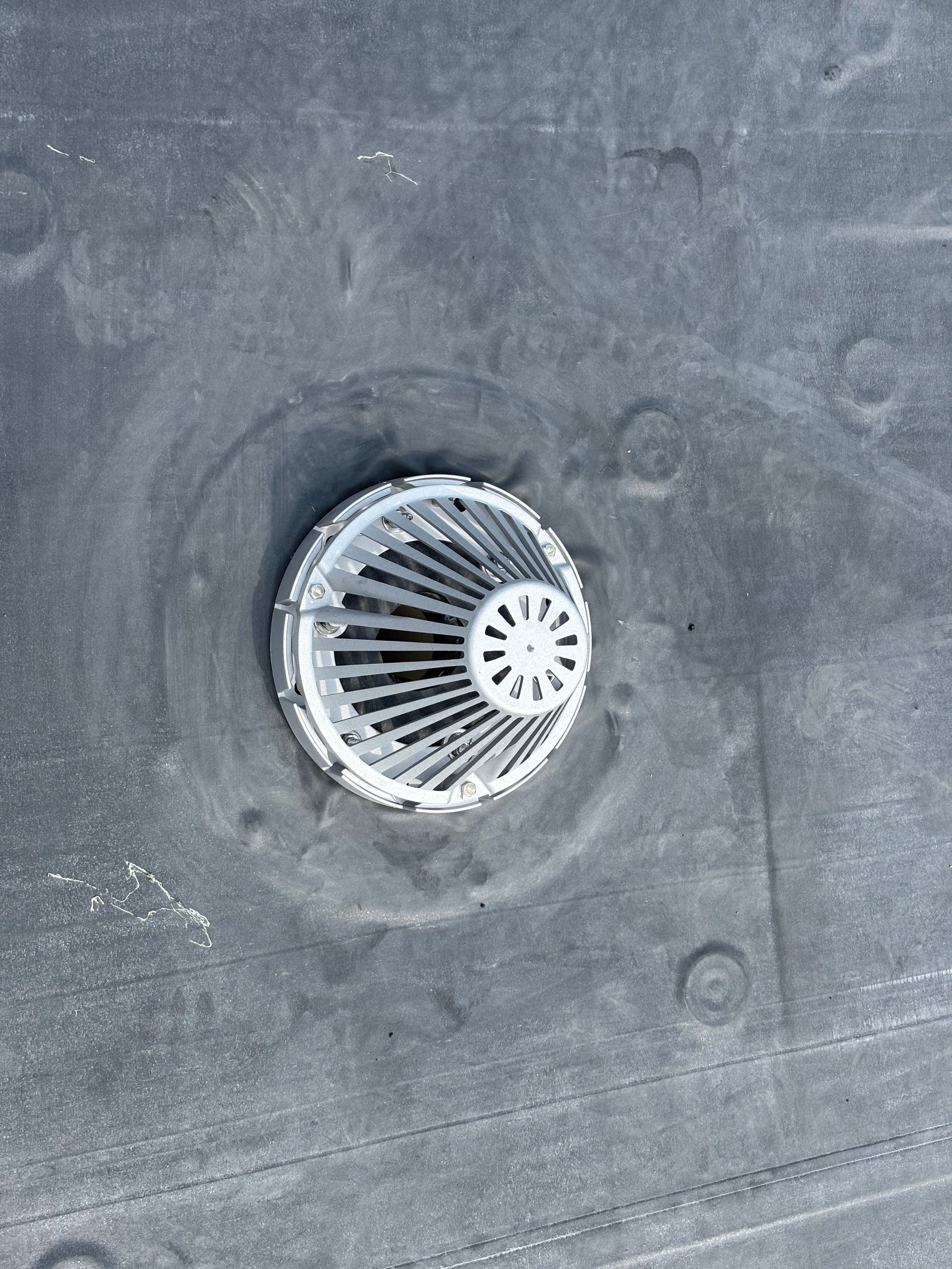 Roof drain with metal strainer on a black roof.