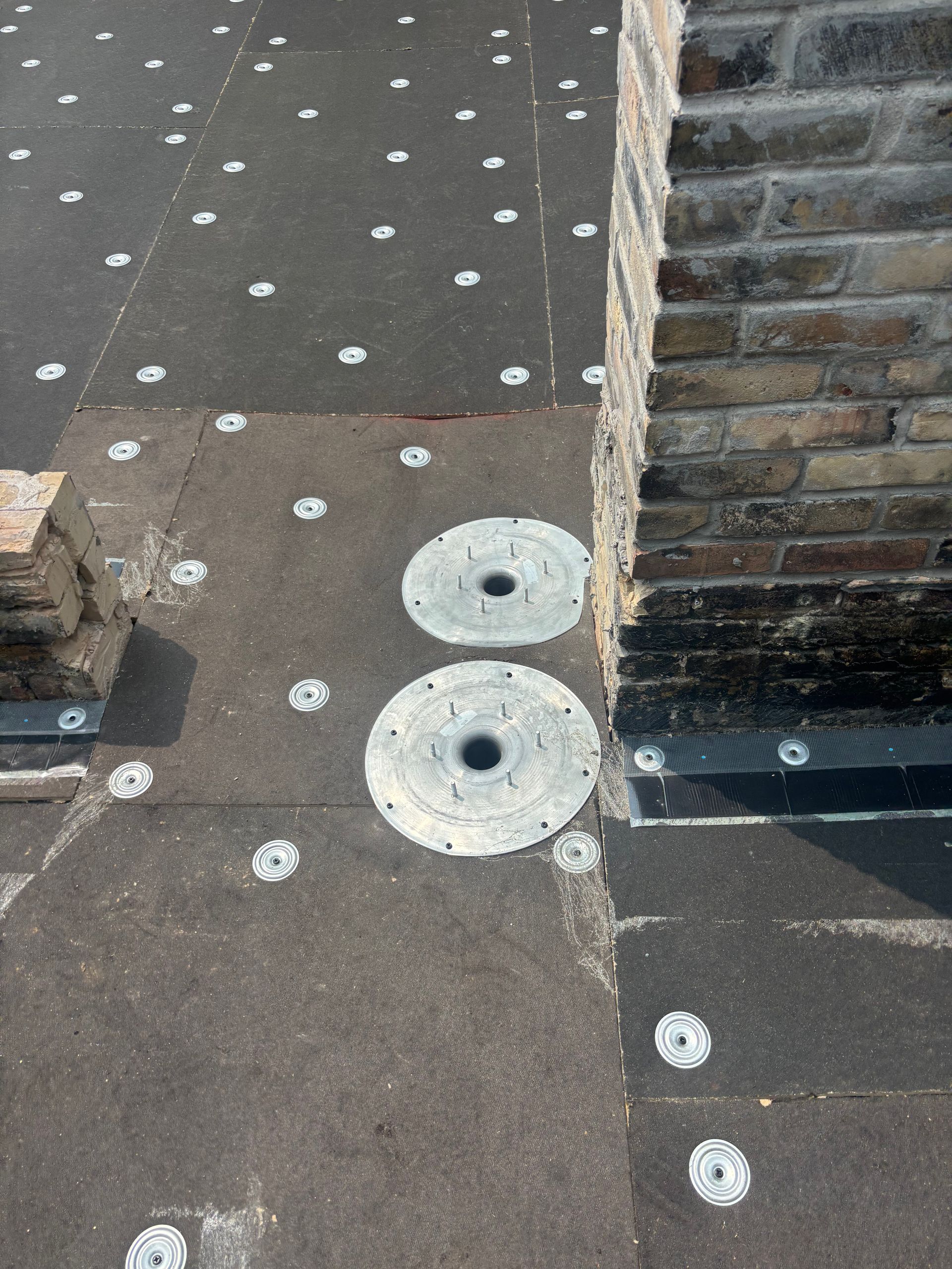 Black roofing with round metal discs and a brick chimney.