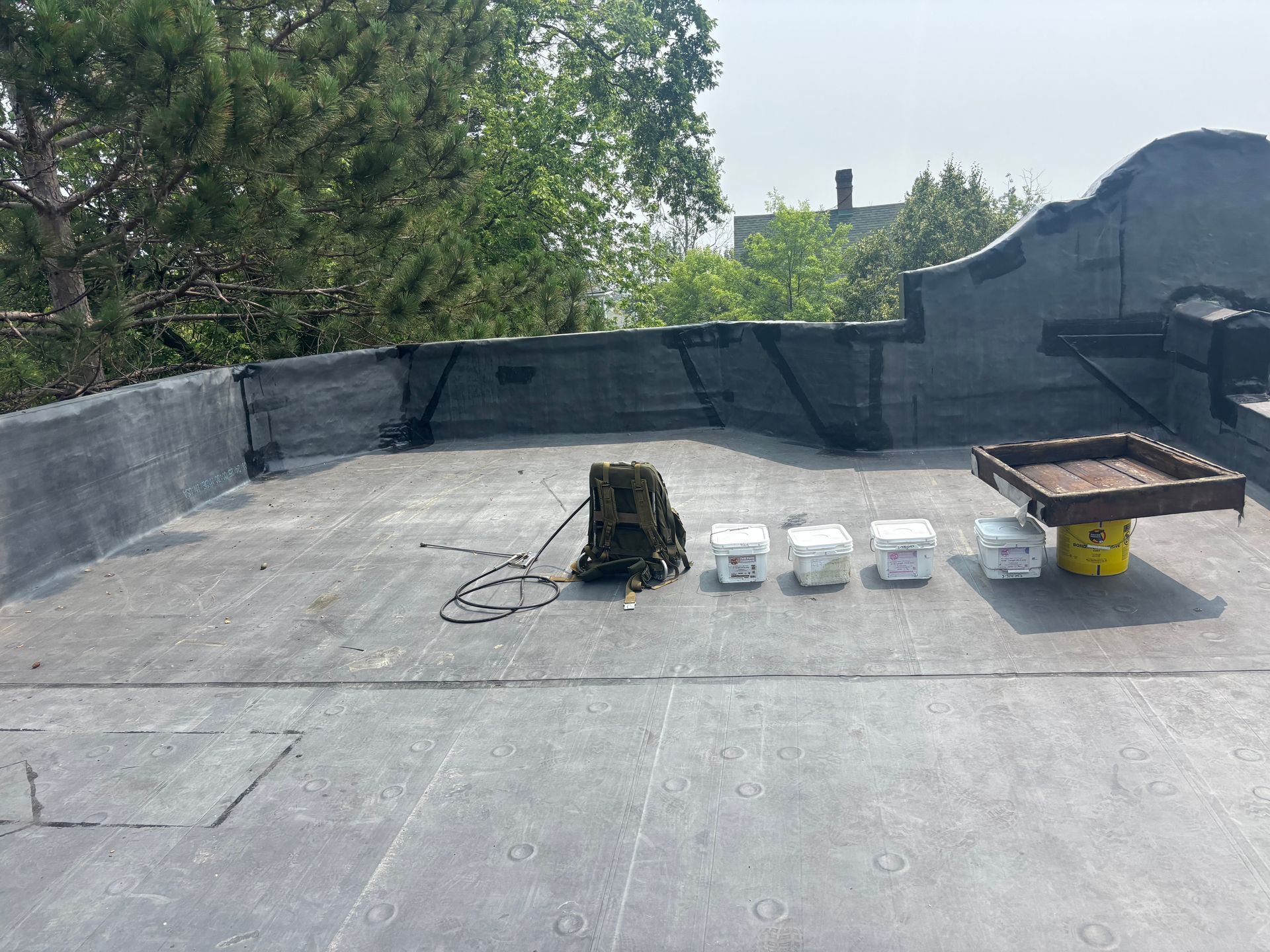 Flat roof with paint buckets, a container, and a rope. Trees and a building are in the background.
