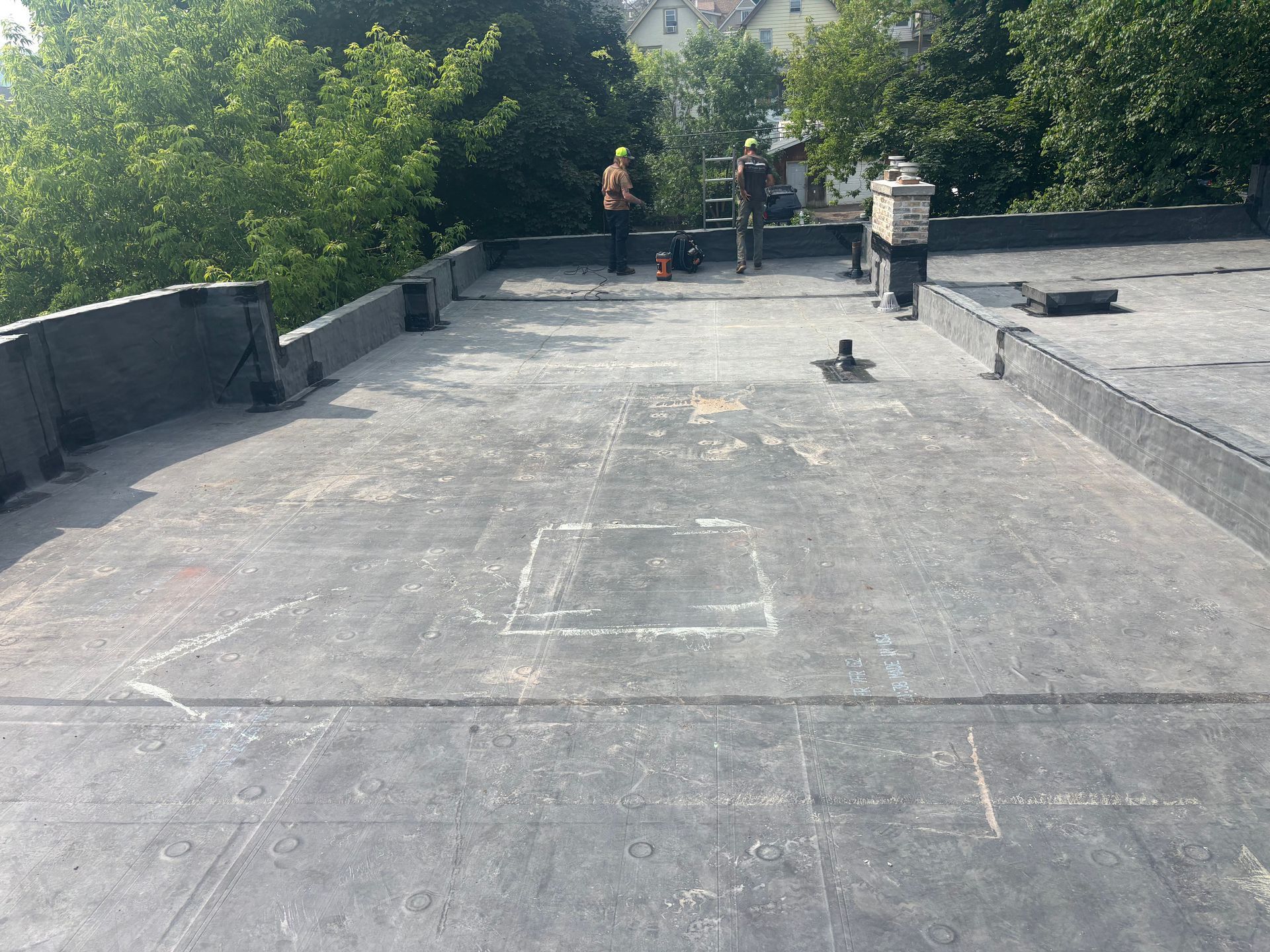 Workers on a flat roof with trees in the background, preparing for a repair.