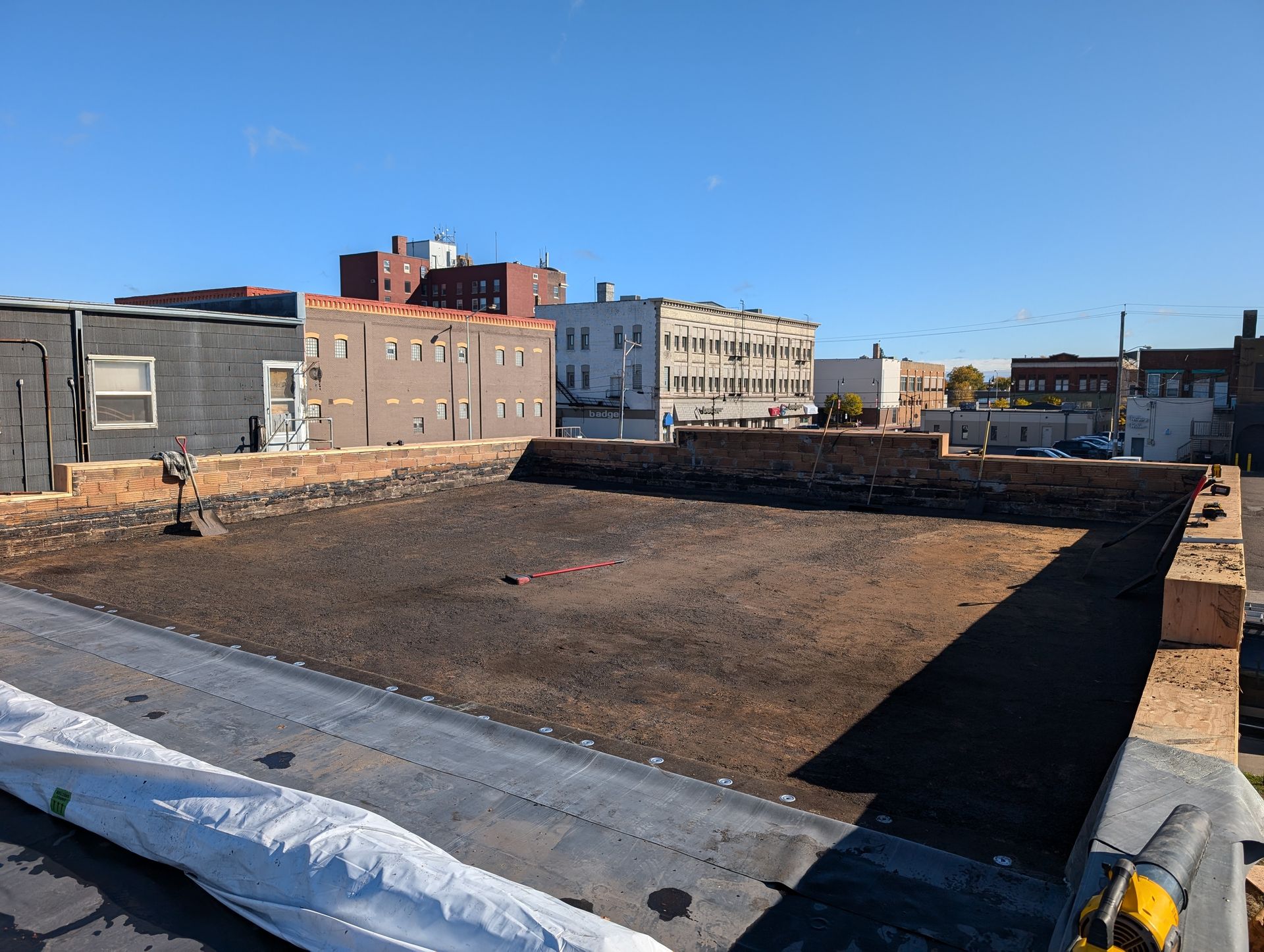 Rooftop with dark surface, brick border, and buildings in the background on a sunny day.