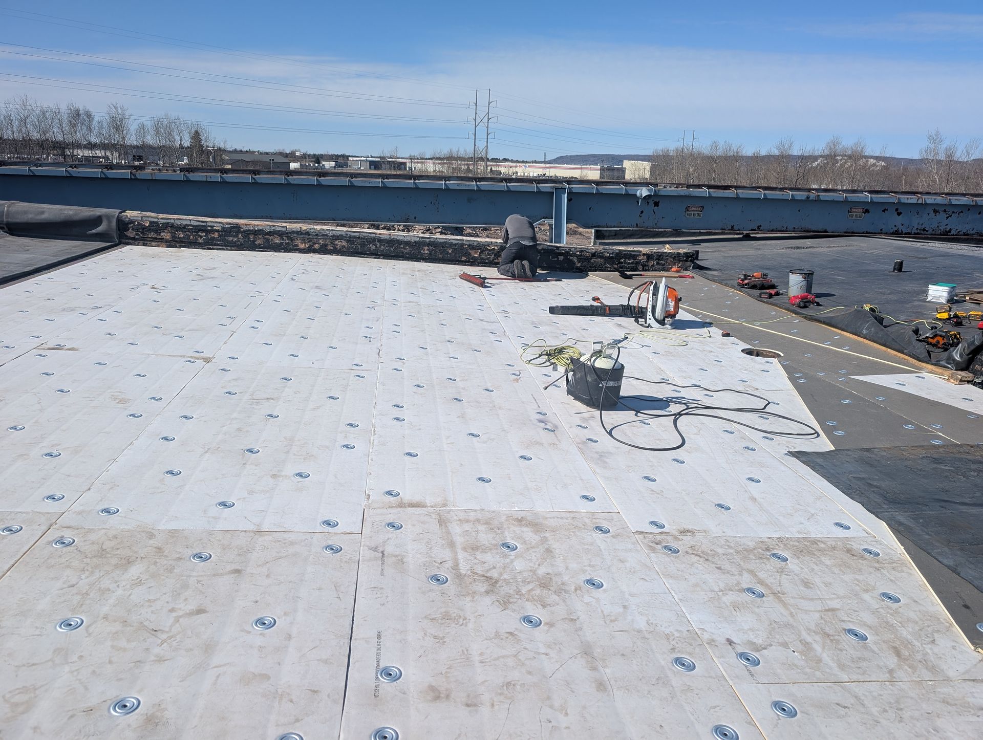 Flat roof partially covered with white insulation and black roofing material. Tools and equipment scattered about.